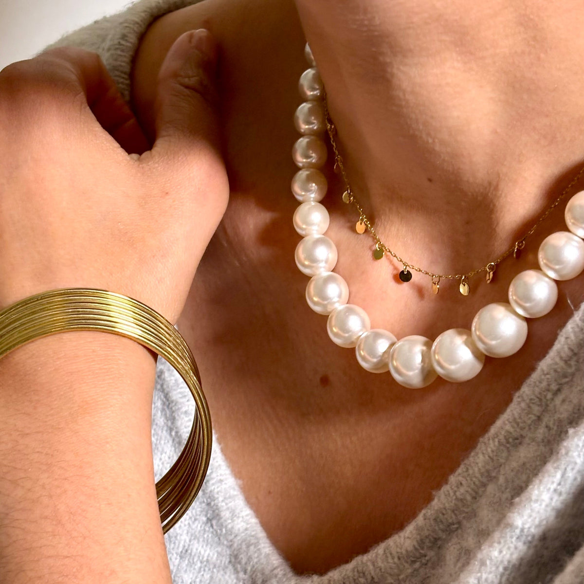 Collier de grosses perles blanches en résine porté avec une chaîne dorée à petits disques et plusieurs joncs dorés