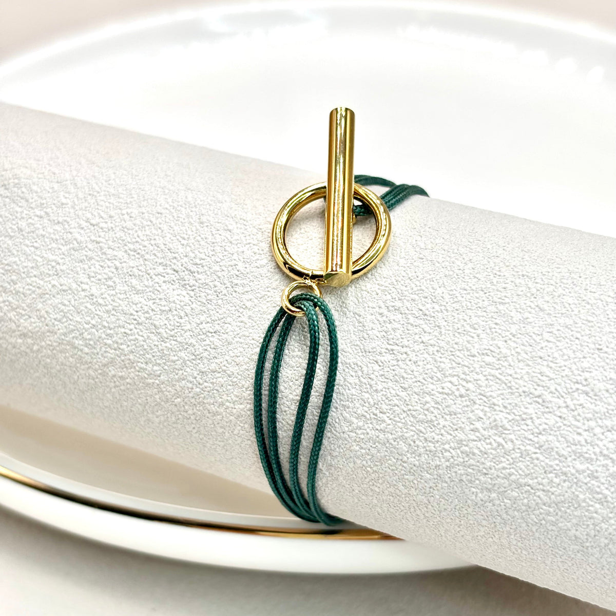Bracelet cordon vert à fermoir T doré, présenté sur support blanc