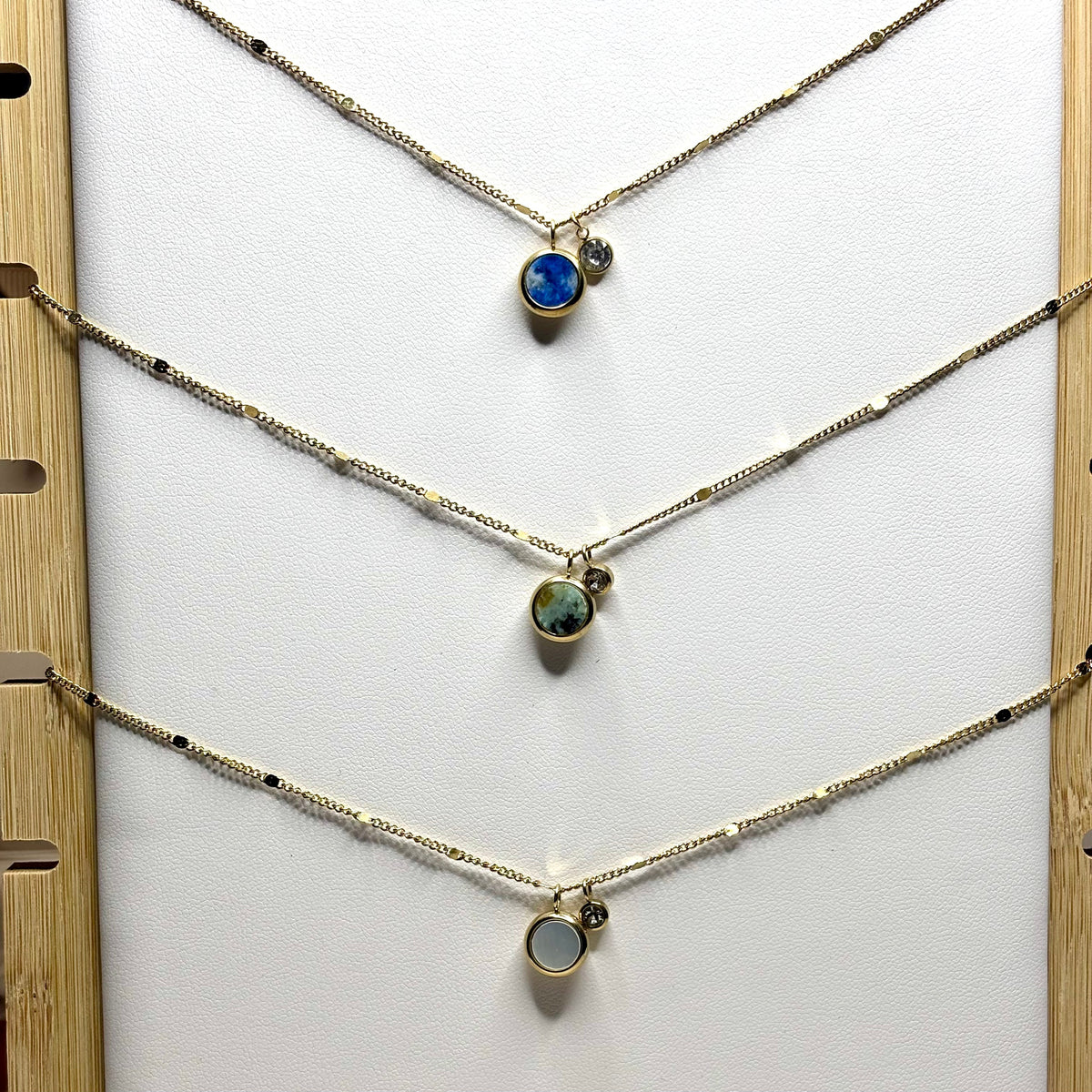 Trois colliers fins dorés avec pendentifs ronds bleu, vert et nacré