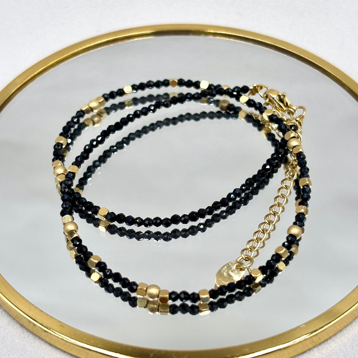 Bracelet en perles d’onyx noir et éléments dorés, présenté sur un miroir