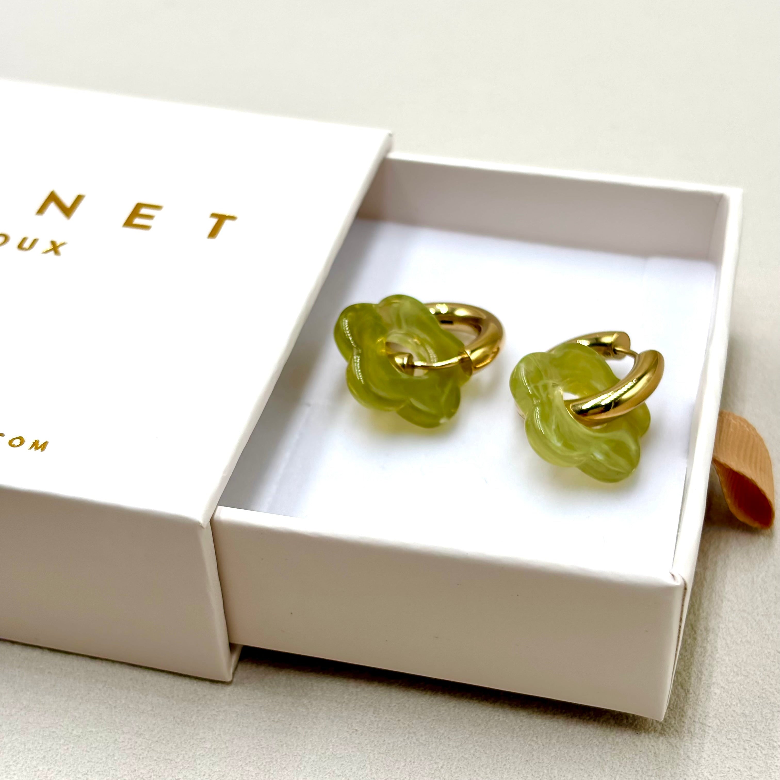 Boucles d'oreilles créoles en acier doré orné d'une fleur en acétate vert clair présentées dans une boite cadeau Djanet Bijoux