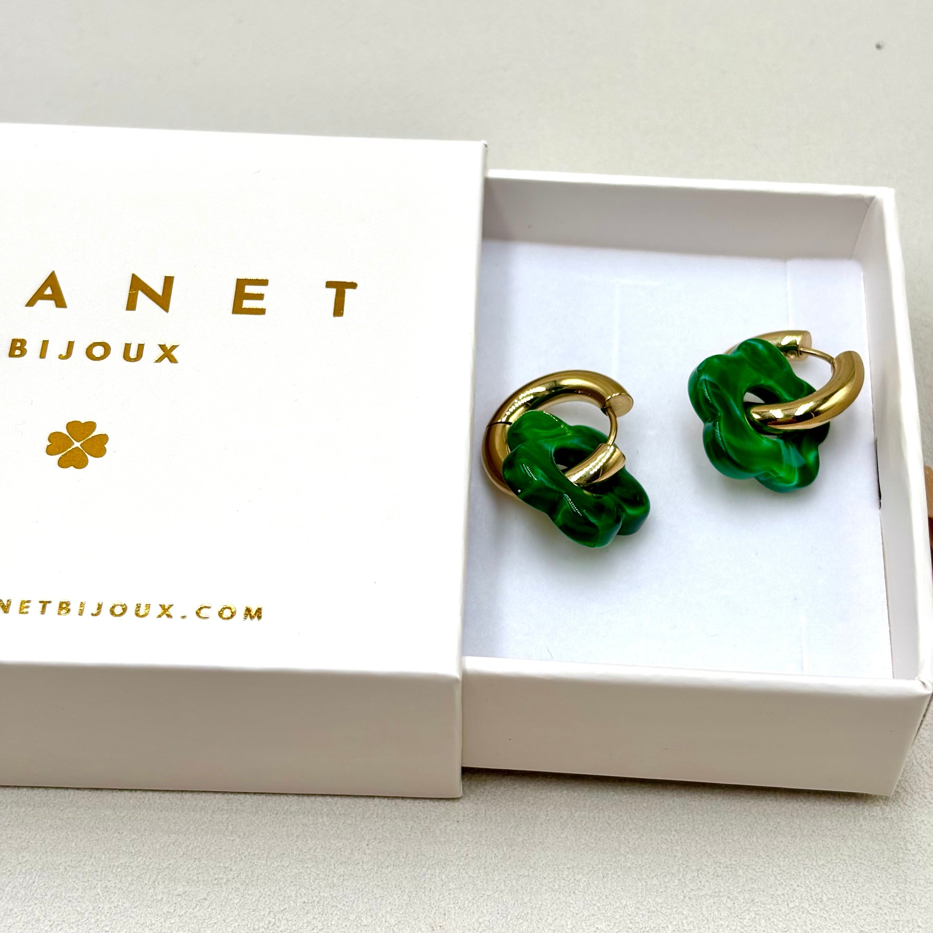 Boucles d'oreilles créoles en acier doré orné d'une fleur en acétate vert foncé présentées dans une boite cadeau Djanet Bijoux