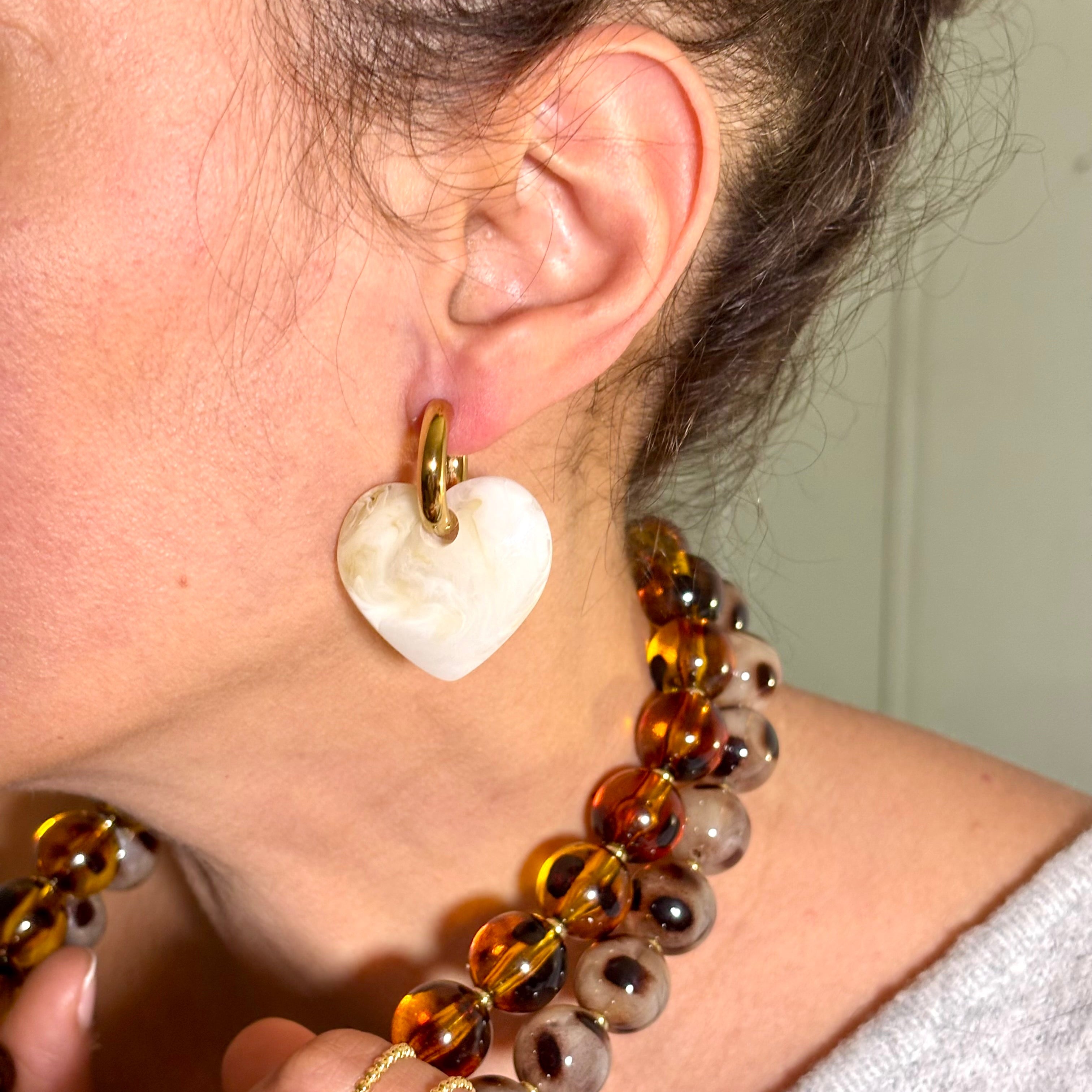 Boucles d'oreilles anneau en acier inoxydable dore et coeur en acétate blanc portées sur l'oreille