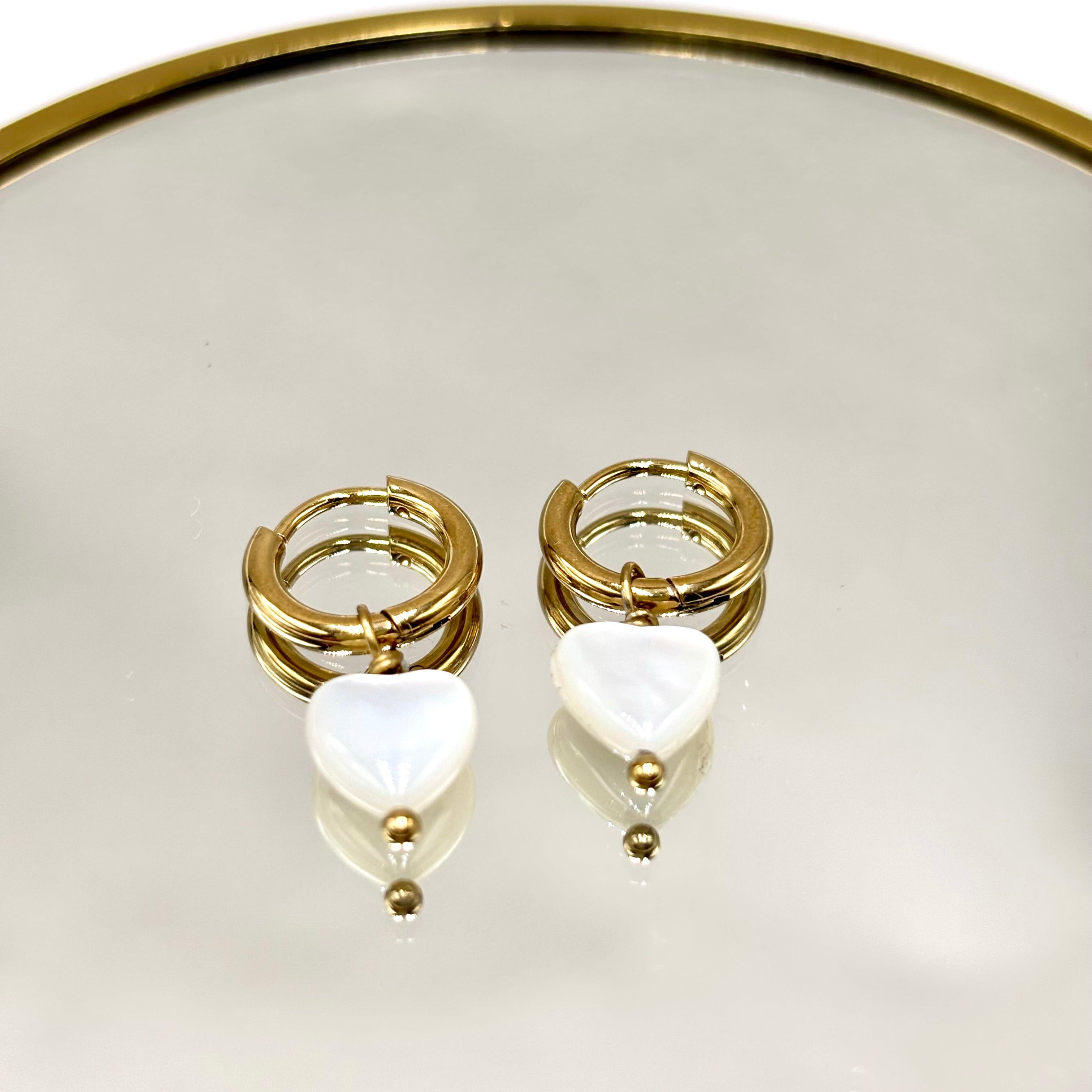 Boucles d'oreilles en acier inoxydable doré et coeur en nacre présenté sur un miroir