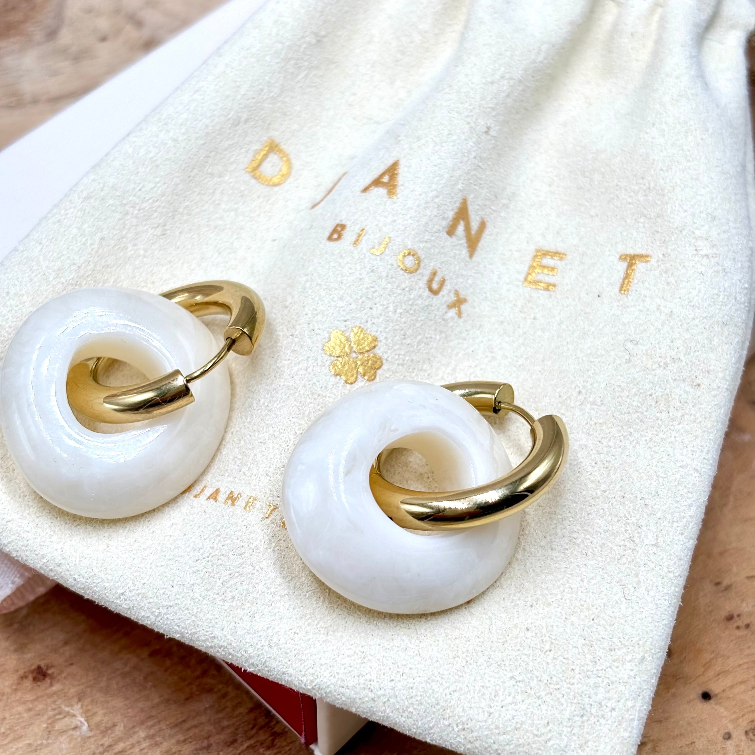 Boucles d'oreilles créoles en acier inoxydable doré et anneaux en forme de donut en acétate coloré blanc ivoire présenté sur pochon Djanet bijoux
