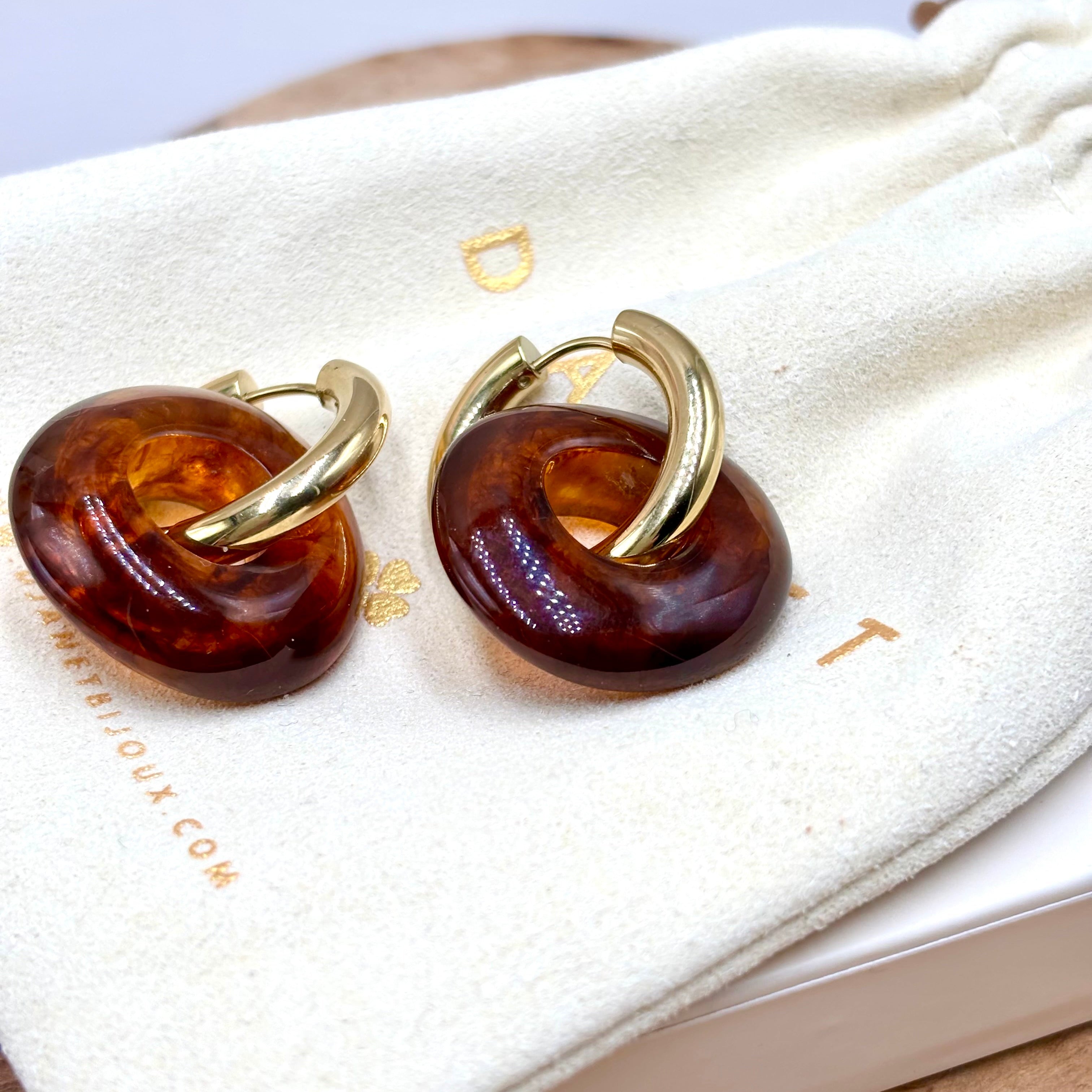 Boucles d'oreilles créoles en acier inoxydable doré et anneaux en forme de donut en acétate coloré brun marron présenté sur pochon Djanet bijoux