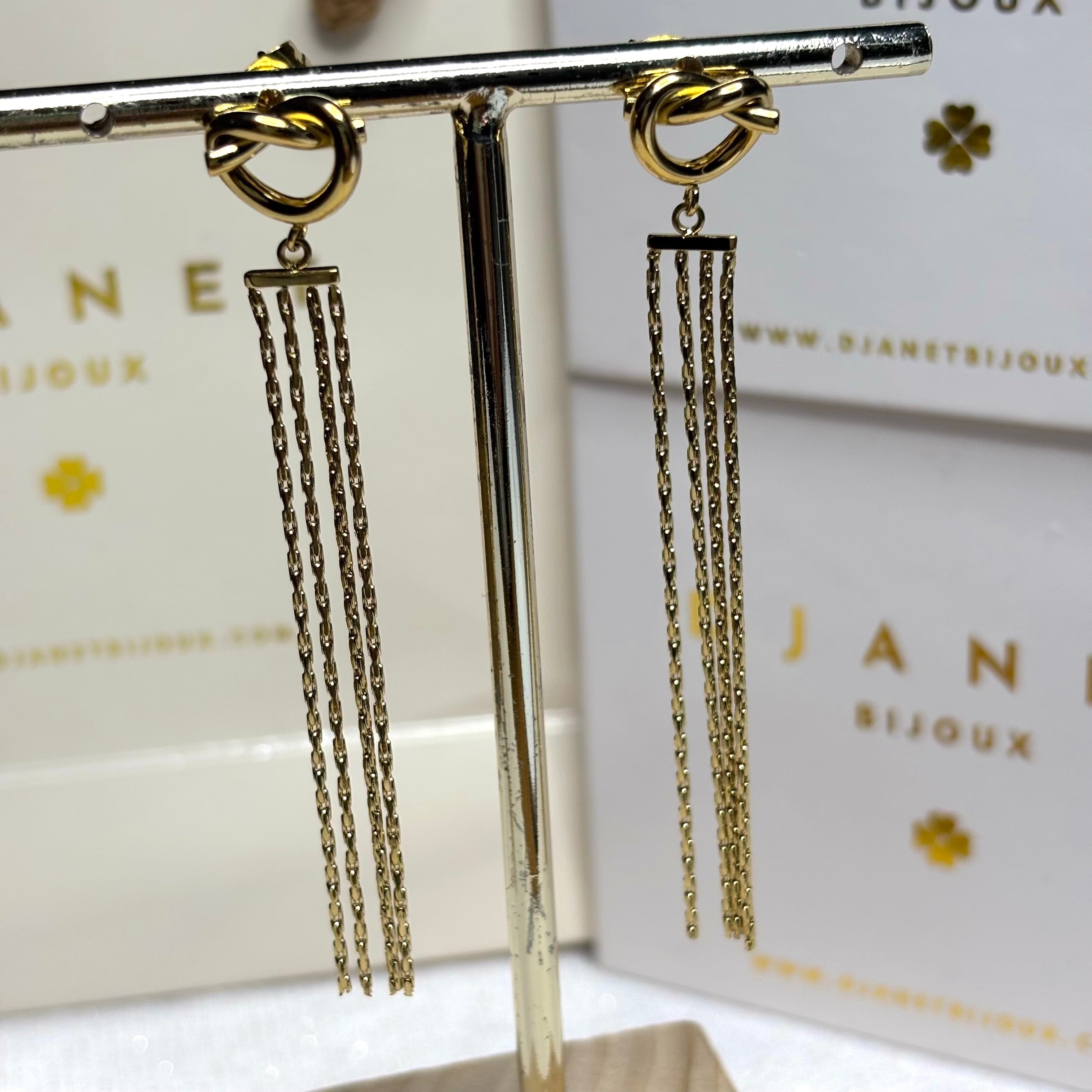 Boucles d'oreilles Giulia en acier inoxydable doré à l'or fin empiecement motif noeud prolongé de 4 petites chaines venitiennes suspendues à un présentoir à bijoux en métal