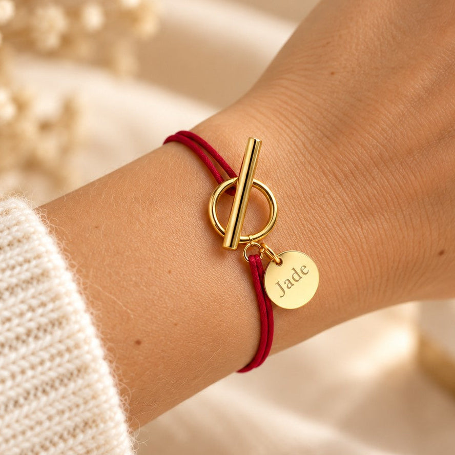 Bracelet cordon rouge bordeaux porté au poignet, fermoir T doré et médaille gravée Jade