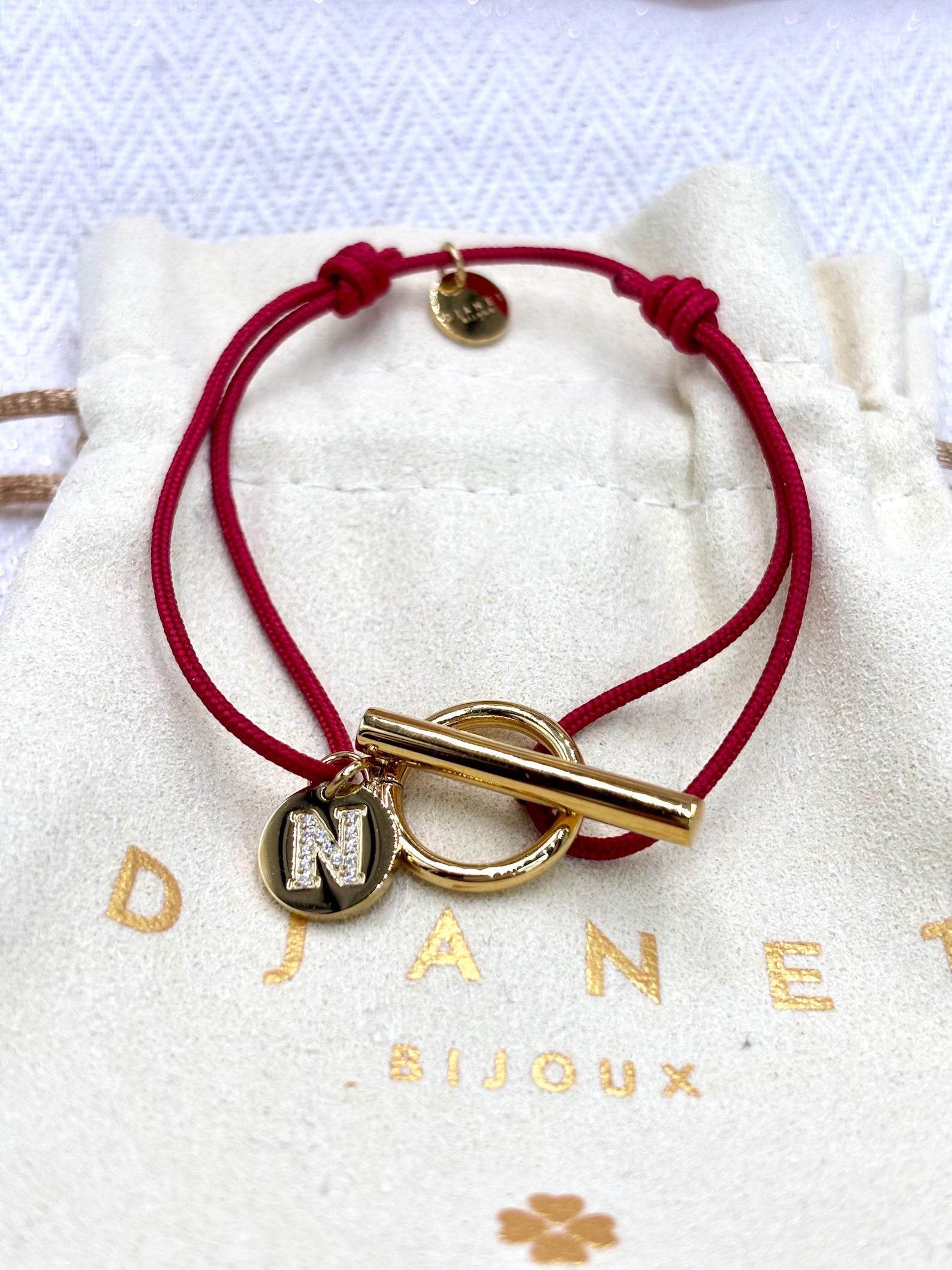 Bracelet cordon rouge fermoir T Toggle et charm lettre zirconium gravée présenté sur pochon Djanet Bijoux