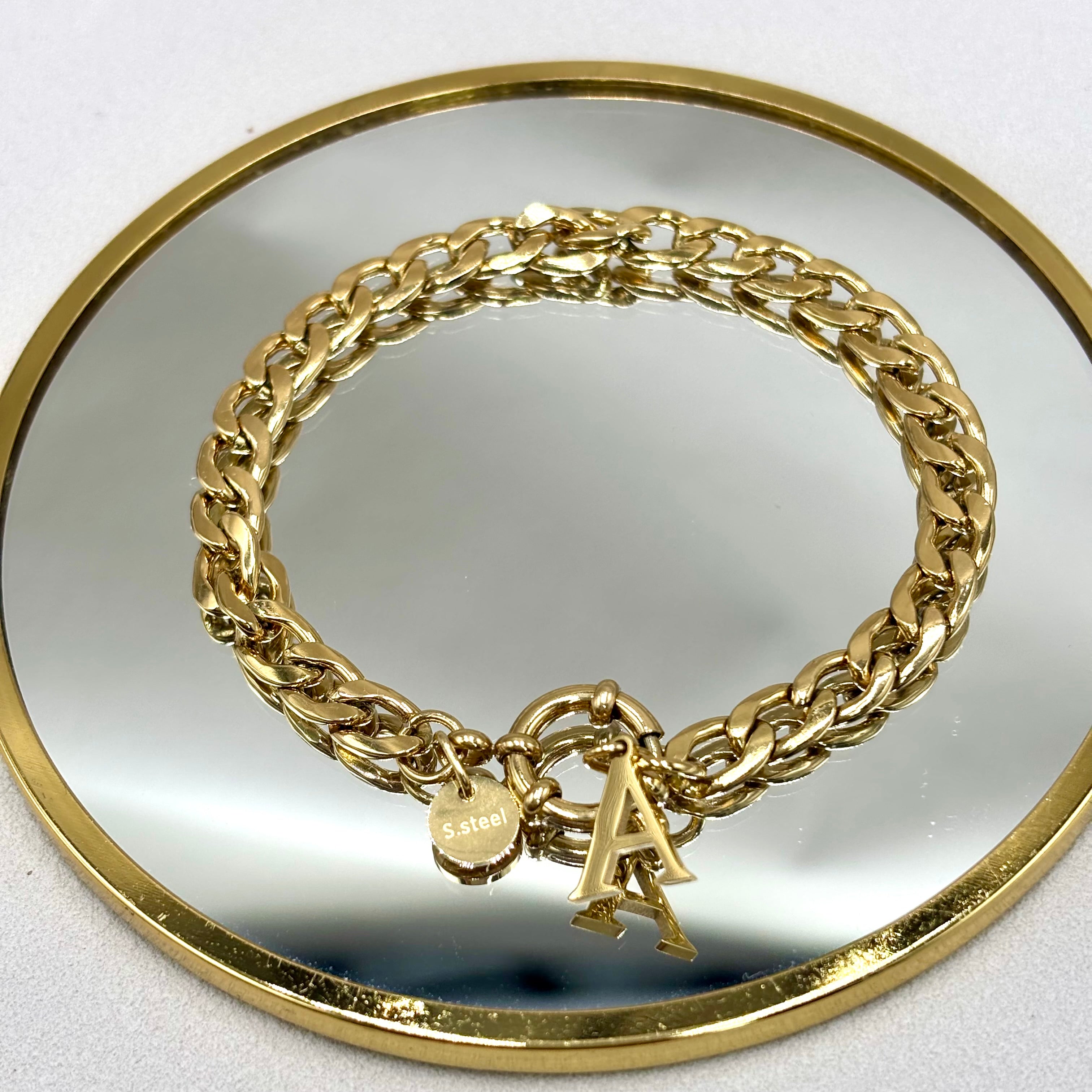 Bracelet gourmette en acier inoxydable doré avec fermoir mousqueton rond bouée et pendentif initiale présenté sur miroir