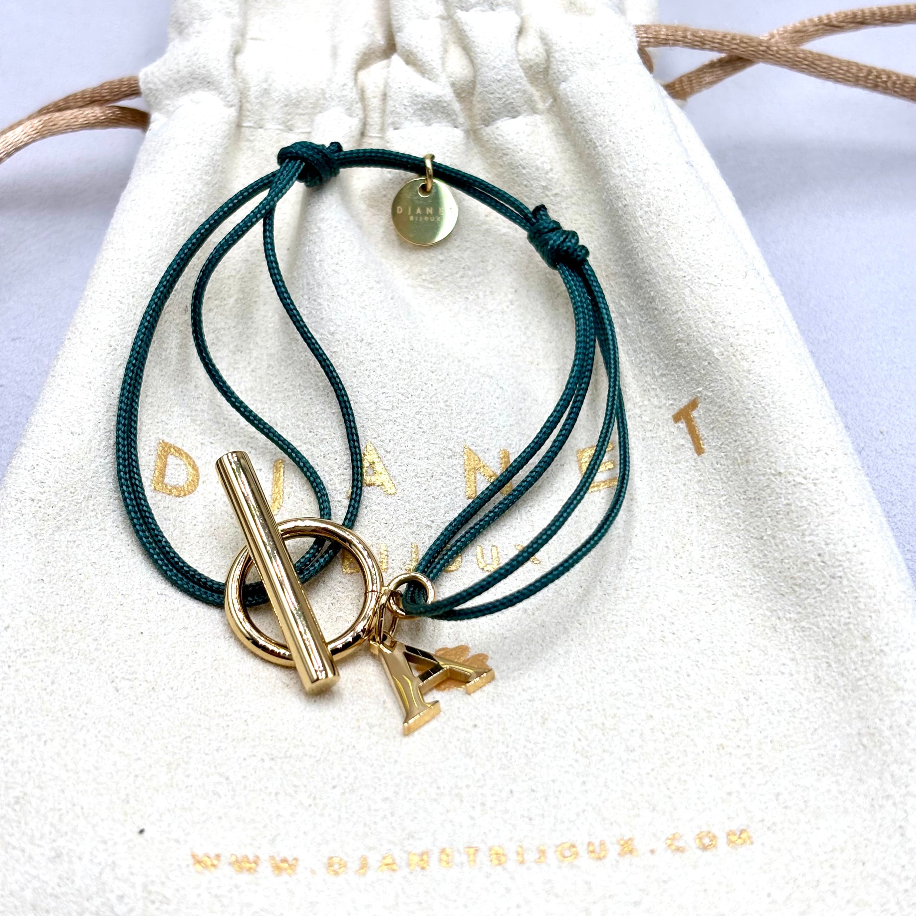 Bracelet double cordon vert personnalise avec lettre initiale fermoir T Toggle en acier inoxydable doré présenté sur pochon Djanet Bijoux
