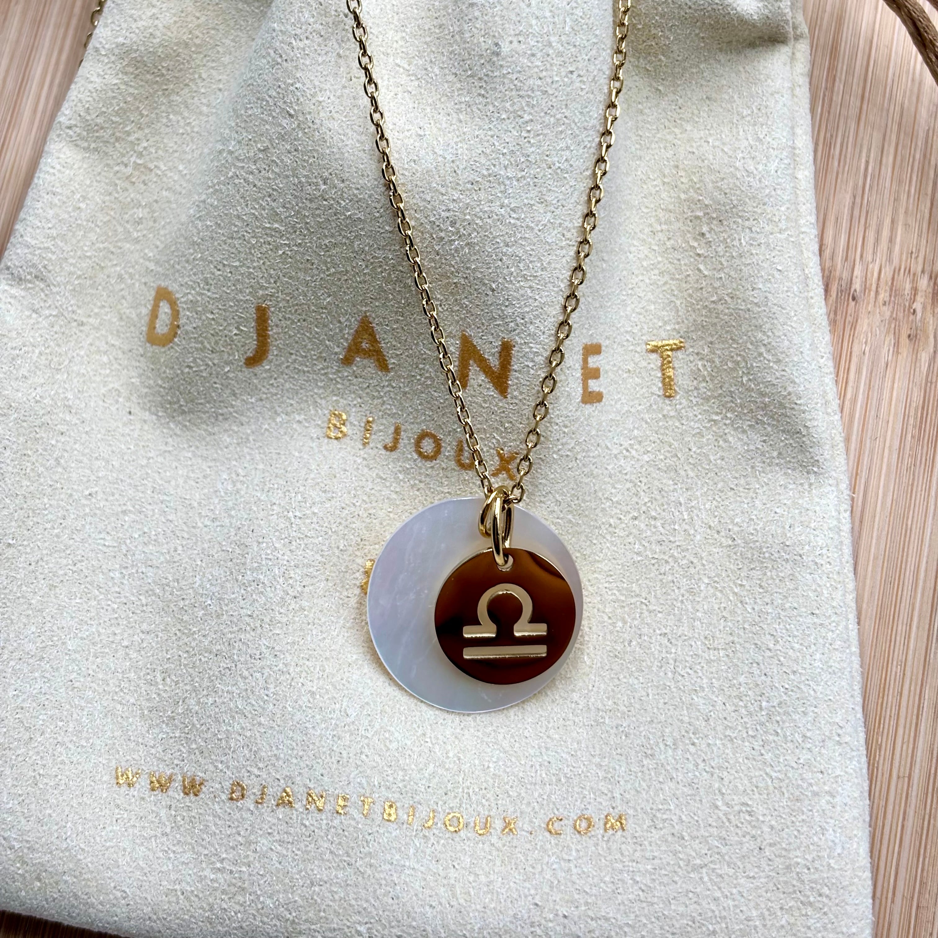 Collier personnalise signe Astro balance sur chaine maille forçat acier dore et medaille ronde en nacre présenté sur pochon Djanet Bijoux