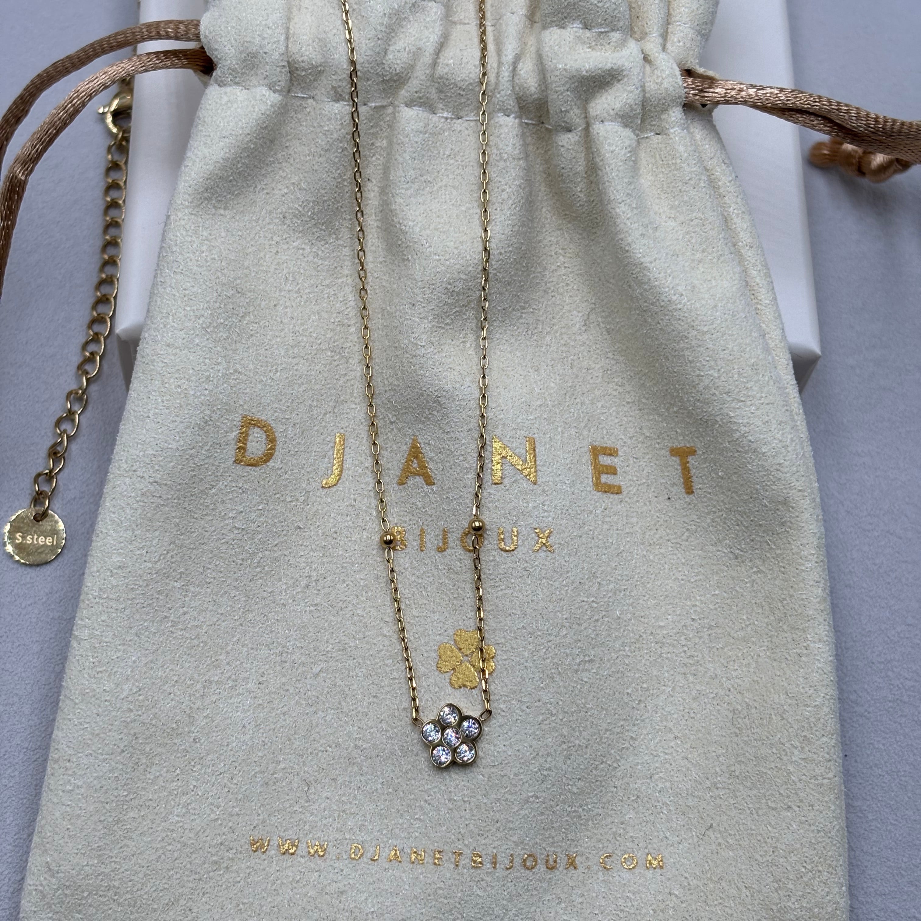 Collier fin en acier inoxydable doré à l'or fin orné d'une fleur en zirconium présenté sur un pochon Djanet Bijoux