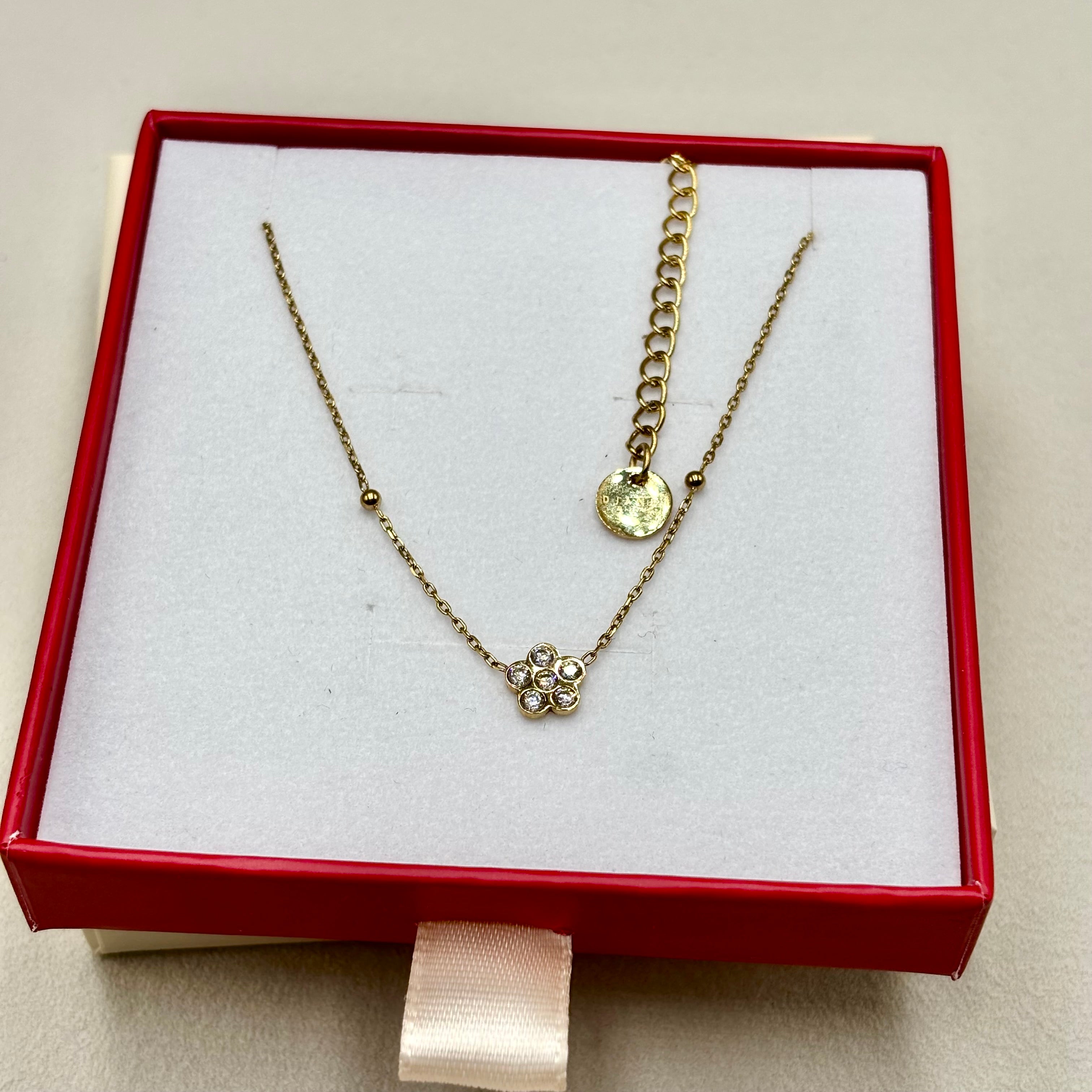 Collier fin orné d'une fleur en zirconium entre deux billes en acier doré présenté sur une boite cadeau Djanet Bijoux