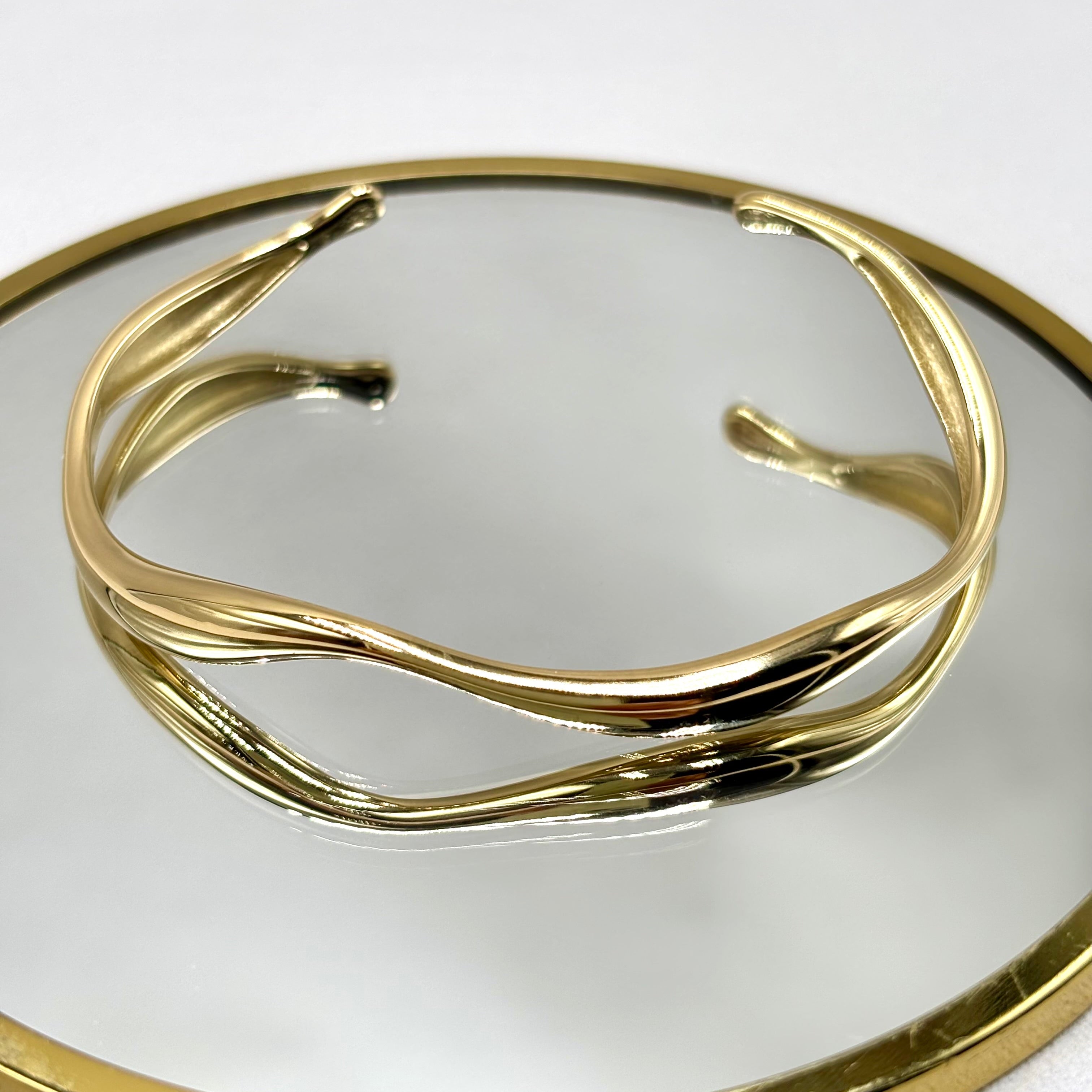 Jonc ondulé ouvert ajustable en acier inoxydable doré sur un miroir