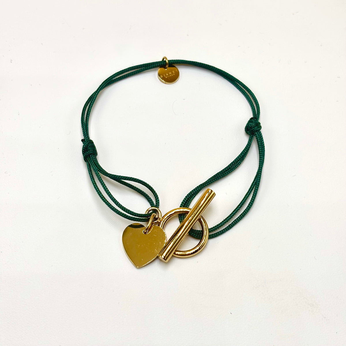 Bracelet cordon vert foncé à nœuds coulissants, fermoir T doré et cœur à graver, présenté à plat.
