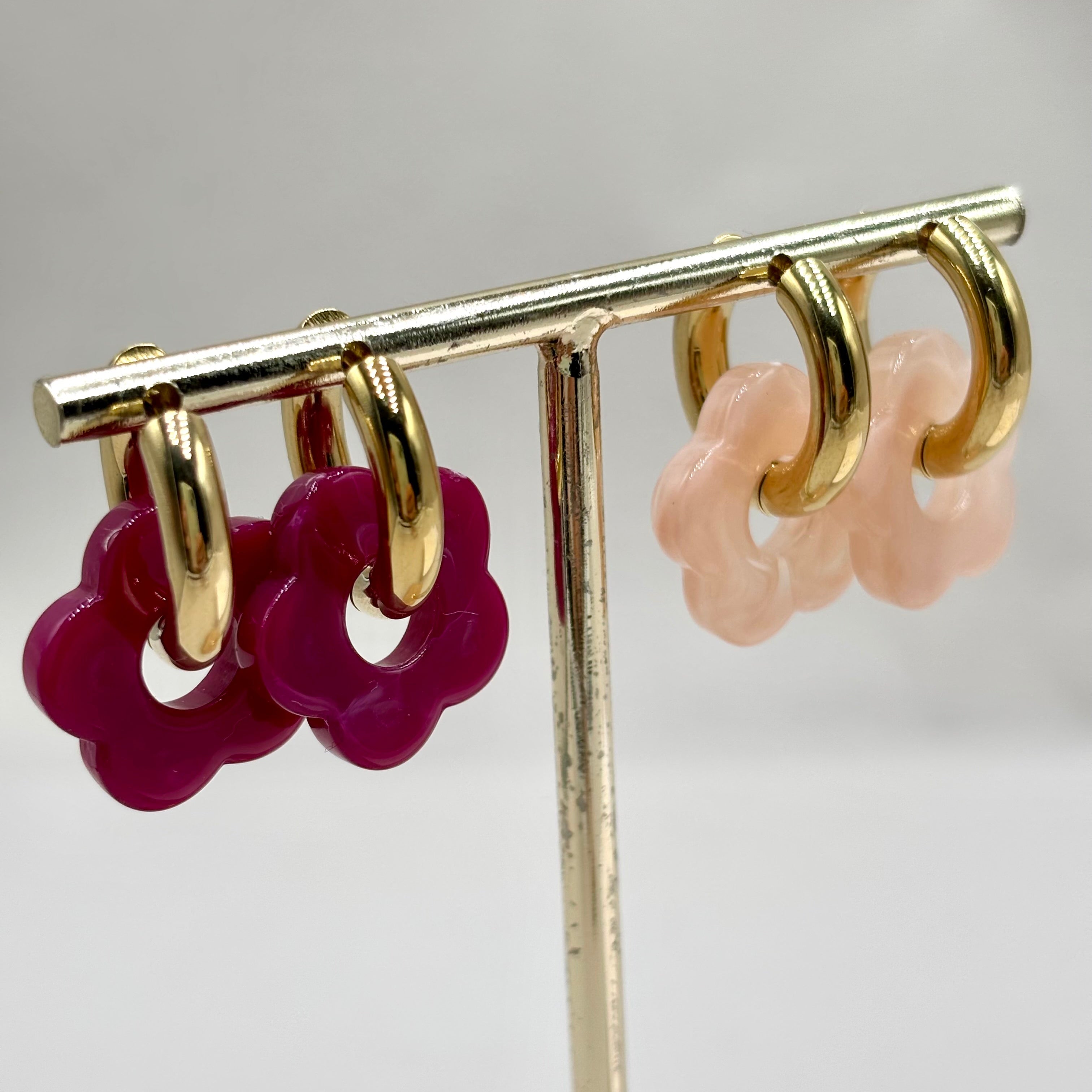 Boucles d'oreilles créoles en acier doré orné d'une fleur en acétate prune et rose clair sur présentoir