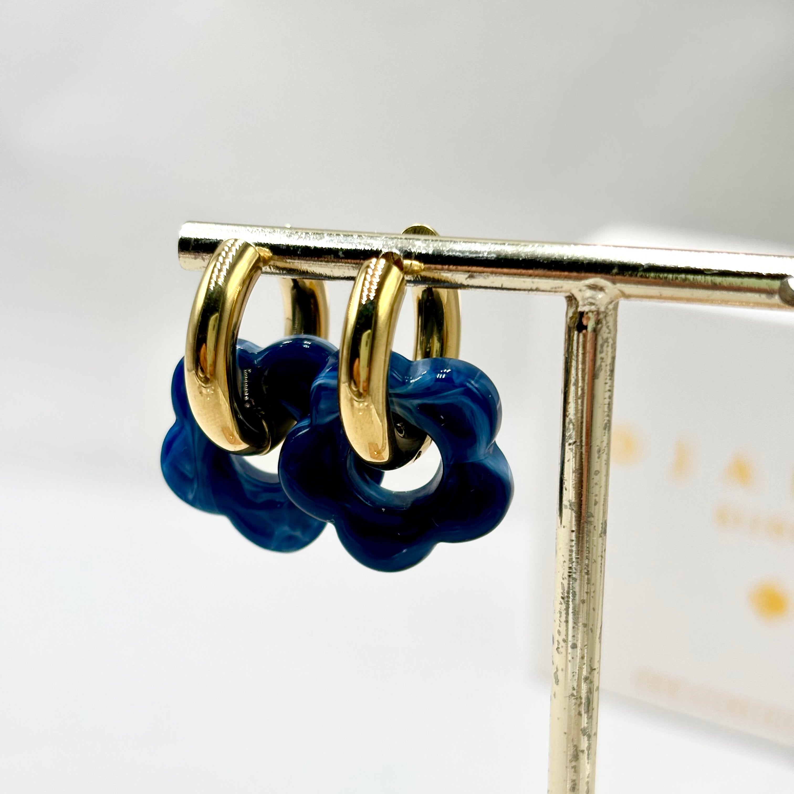 Boucles d'oreilles créoles en acier doré orné d'une fleur en acétate bleu foncé sur présentoir