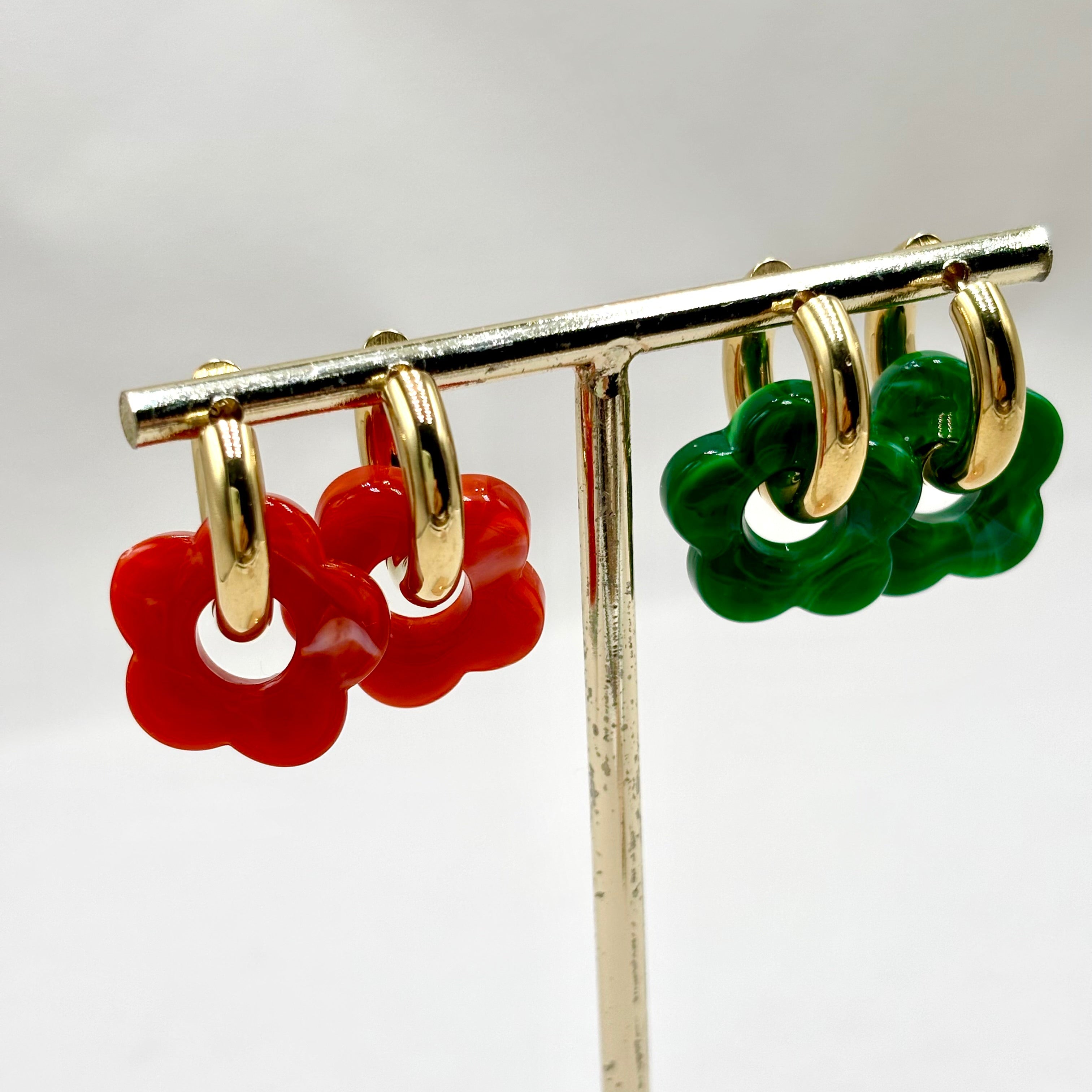 Boucles d'oreilles créoles en acier doré orné d'une fleur en acétate vert foncé et rouge orangé sur présentoir 