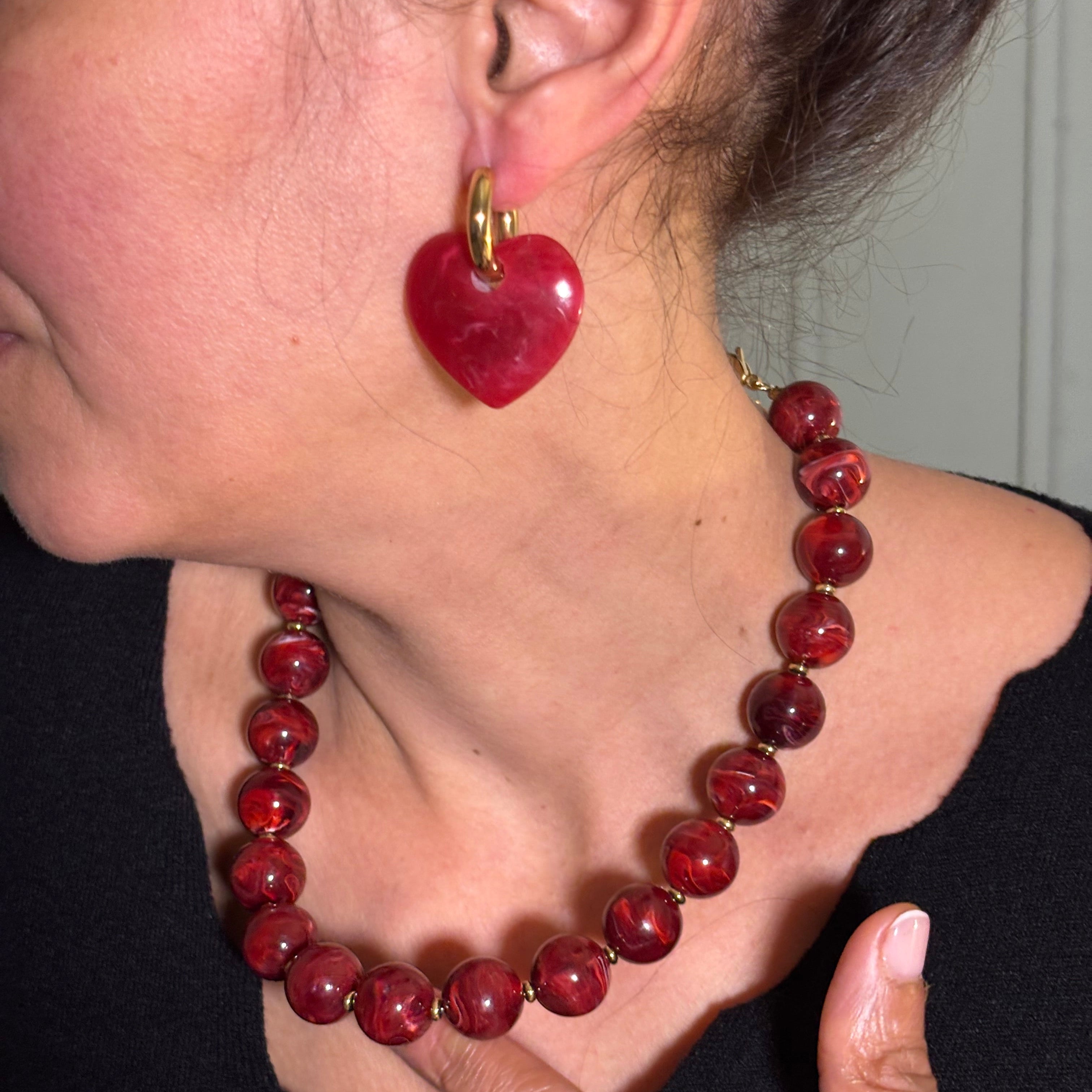 Boucles d'oreilles anneau en acier inoxydable dore et coeur en acétate rouge portées sur l'oreille