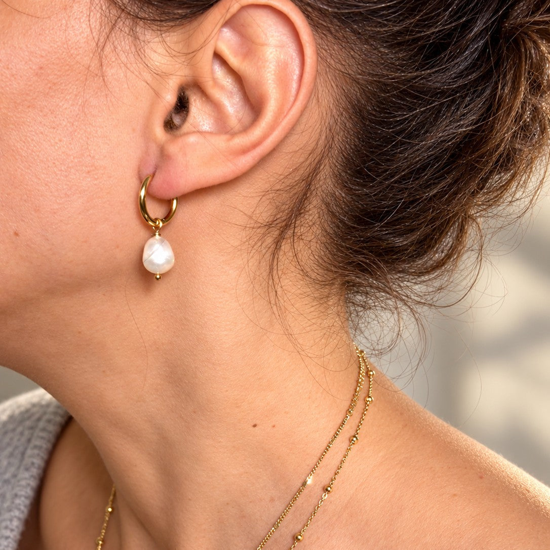 Petite Créole dorée avec perle d’eau douce blanche pendante portée à l’oreille, accompagnée de colliers dorés