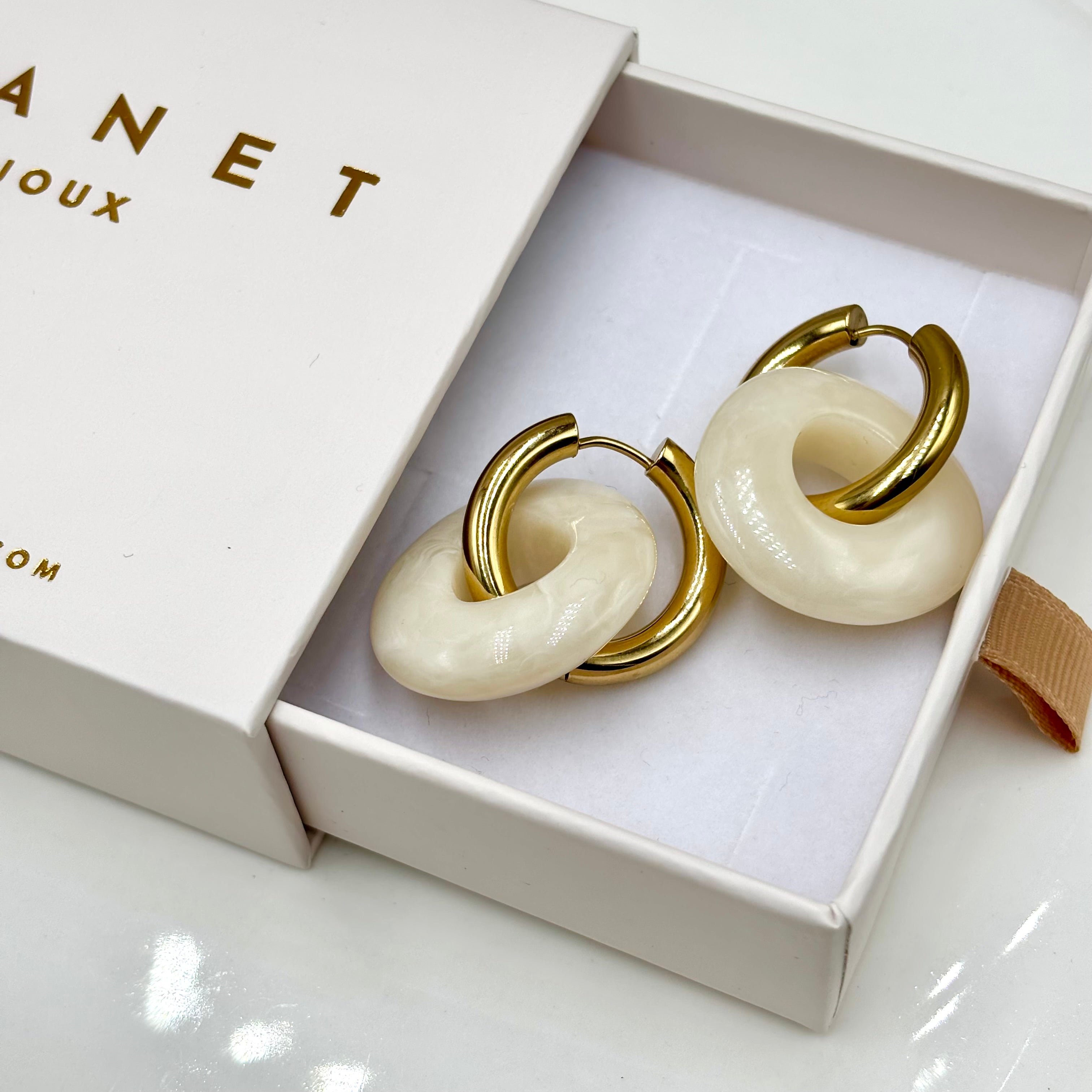 Boucles d'oreilles créoles en acier inoxydable doré et anneaux en forme de donut en acétate coloré blanc ivoire présenté dans boite cadeau Djanet bijoux