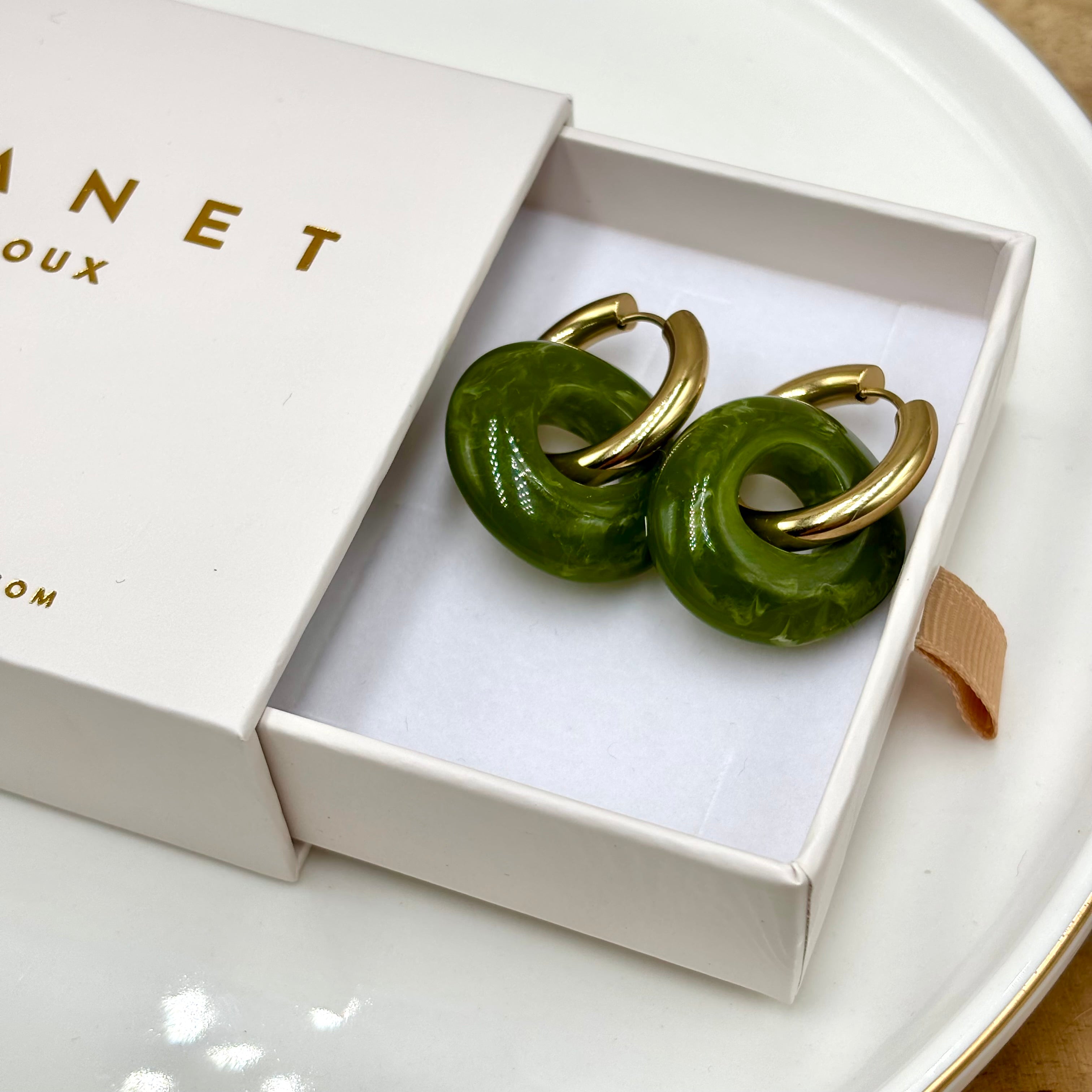 Boucles d'oreilles créoles en acier inoxydable doré et anneaux en forme de donut en acétate coloré vert kaki présenté dans boite cadeau Djanet bijoux