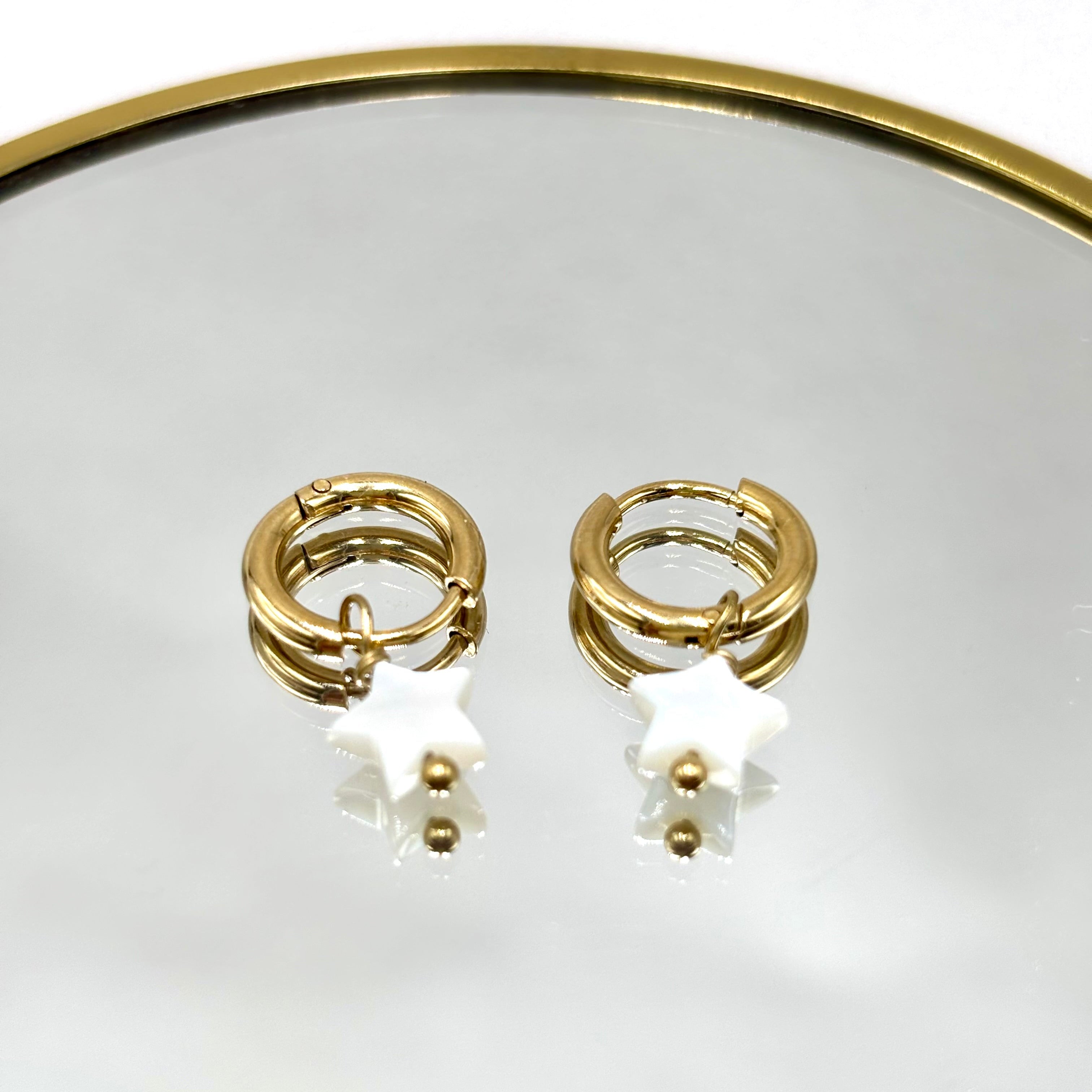 Boucles d'oreilles mini créoles en acier inoxydable doré et étoile en nacre blanche présentées sur miroir