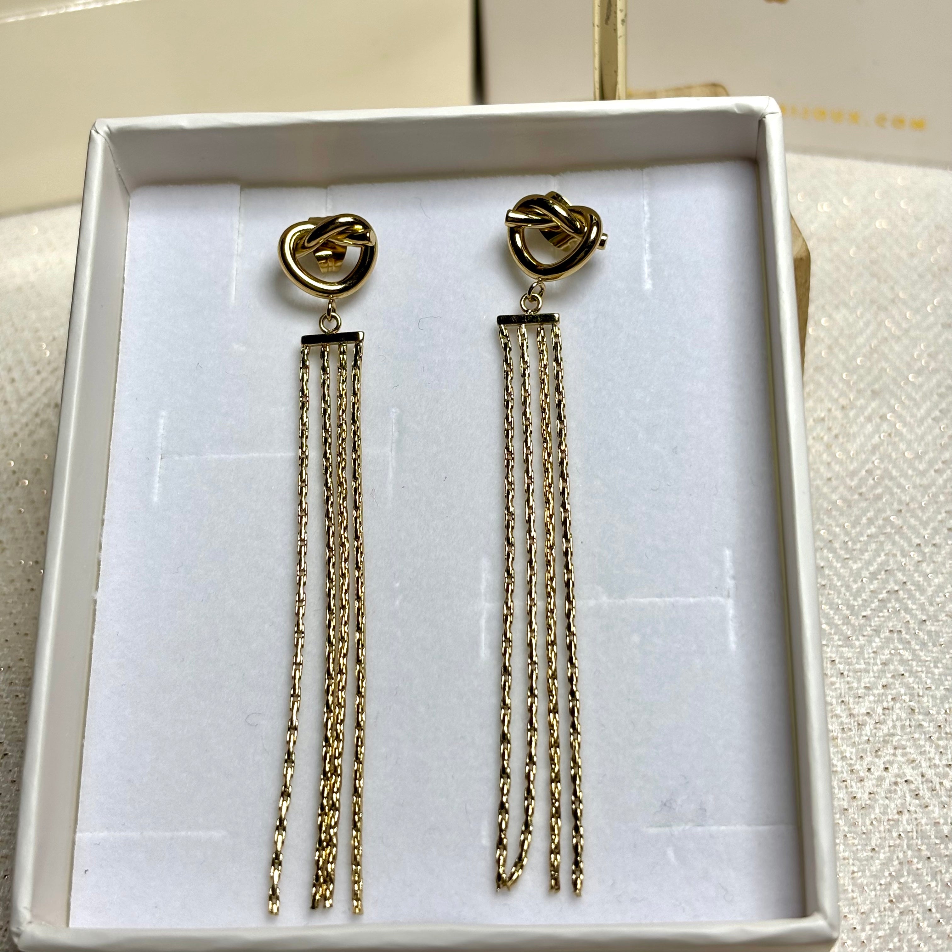 Boucles d'oreilles pendantes noeud et chaines fines vénitiennes en acier inoxydable doré à l'or fin Giulia présentées dans boite tiroir à bijoux