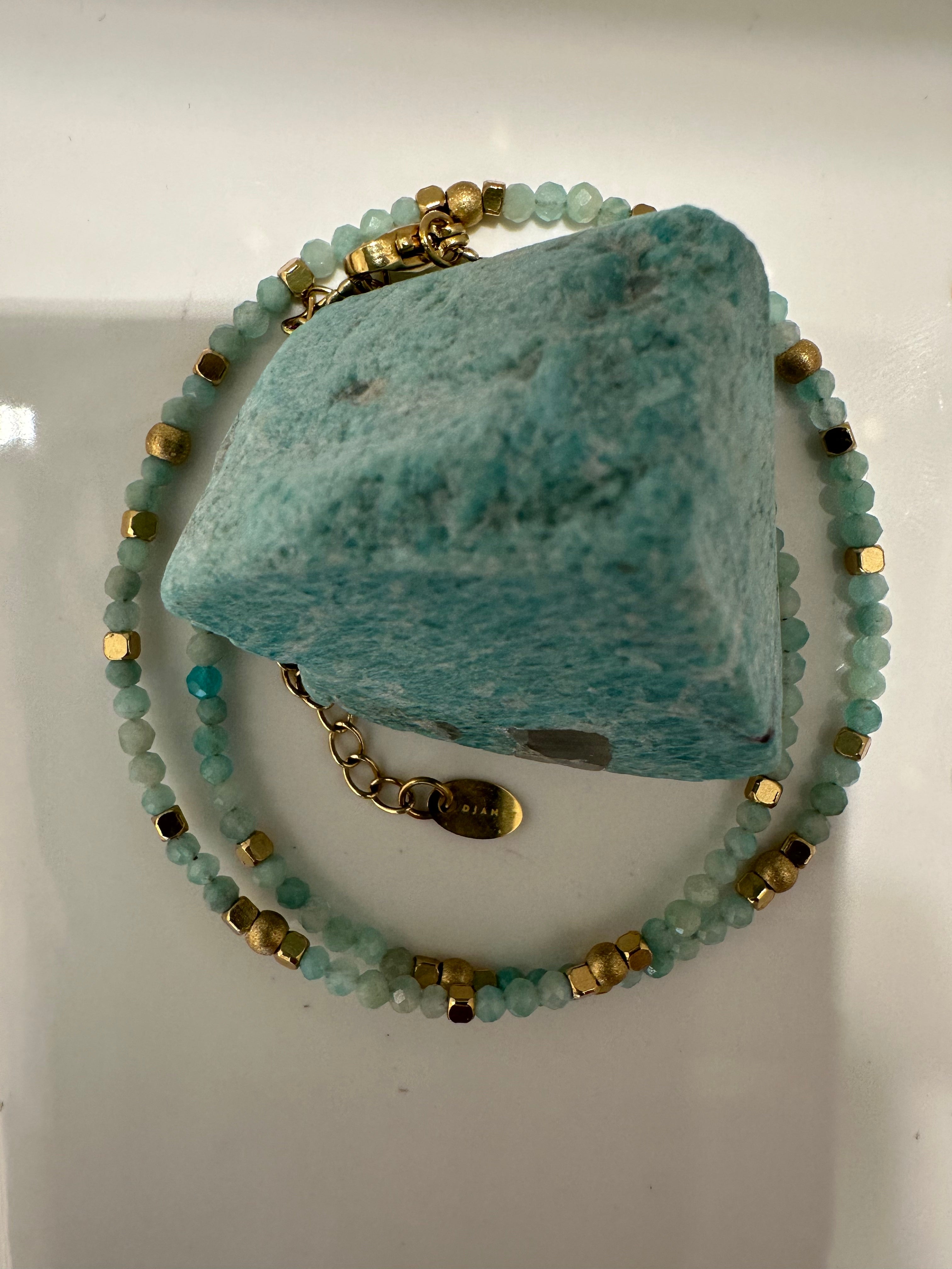 Bracelet amazonite hématites dorées double tours présenté autour d'une pierre brute d'amazonite
