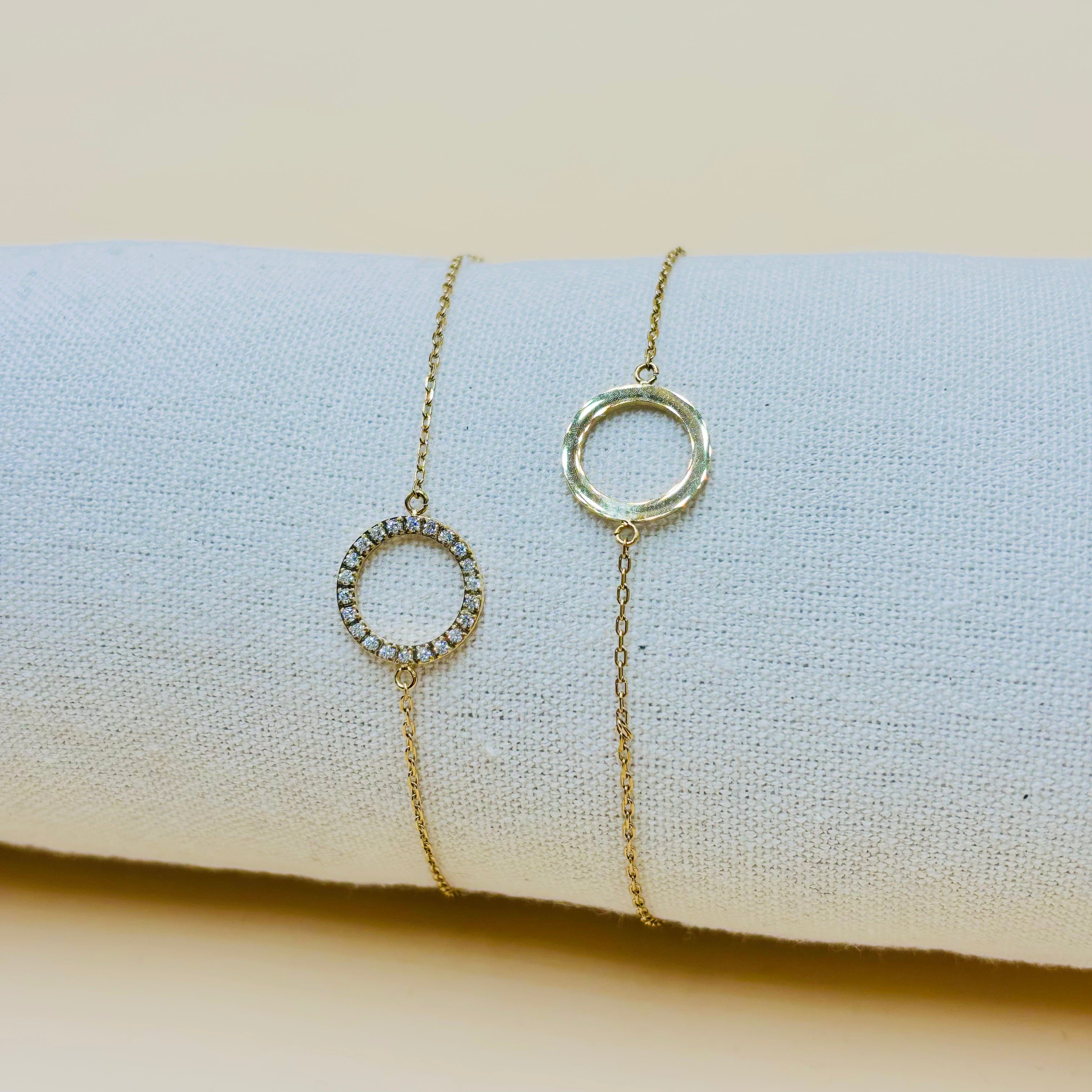 Front and back views of the gold-tone Aura bracelet, with a cubic zirconia-set open circle and fine chain, on light fabric.