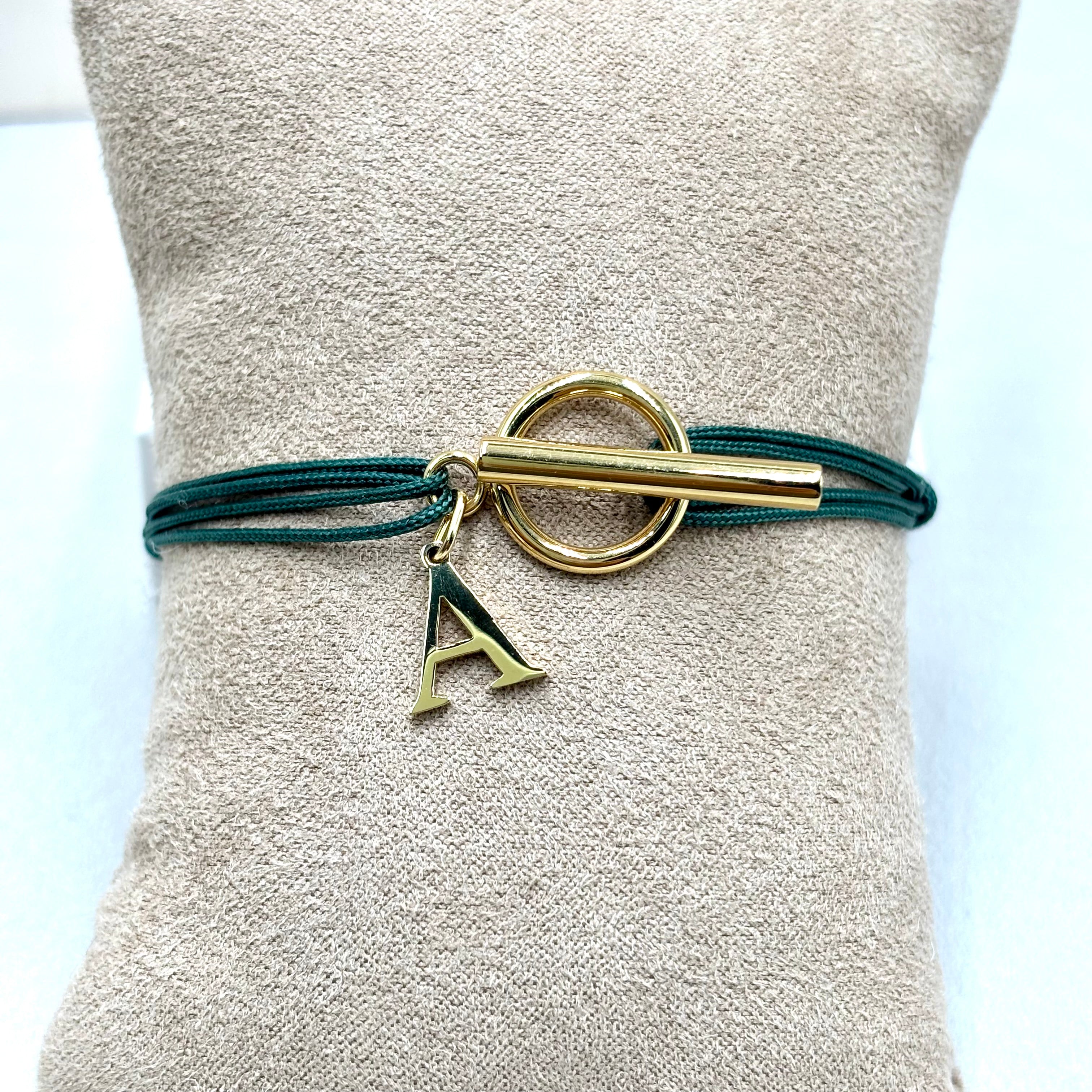 Bracelet double cordon vert  personnalise avec lettre initiale fermoir T Toggle en acier inoxydable dore sur un présentoir coussin 