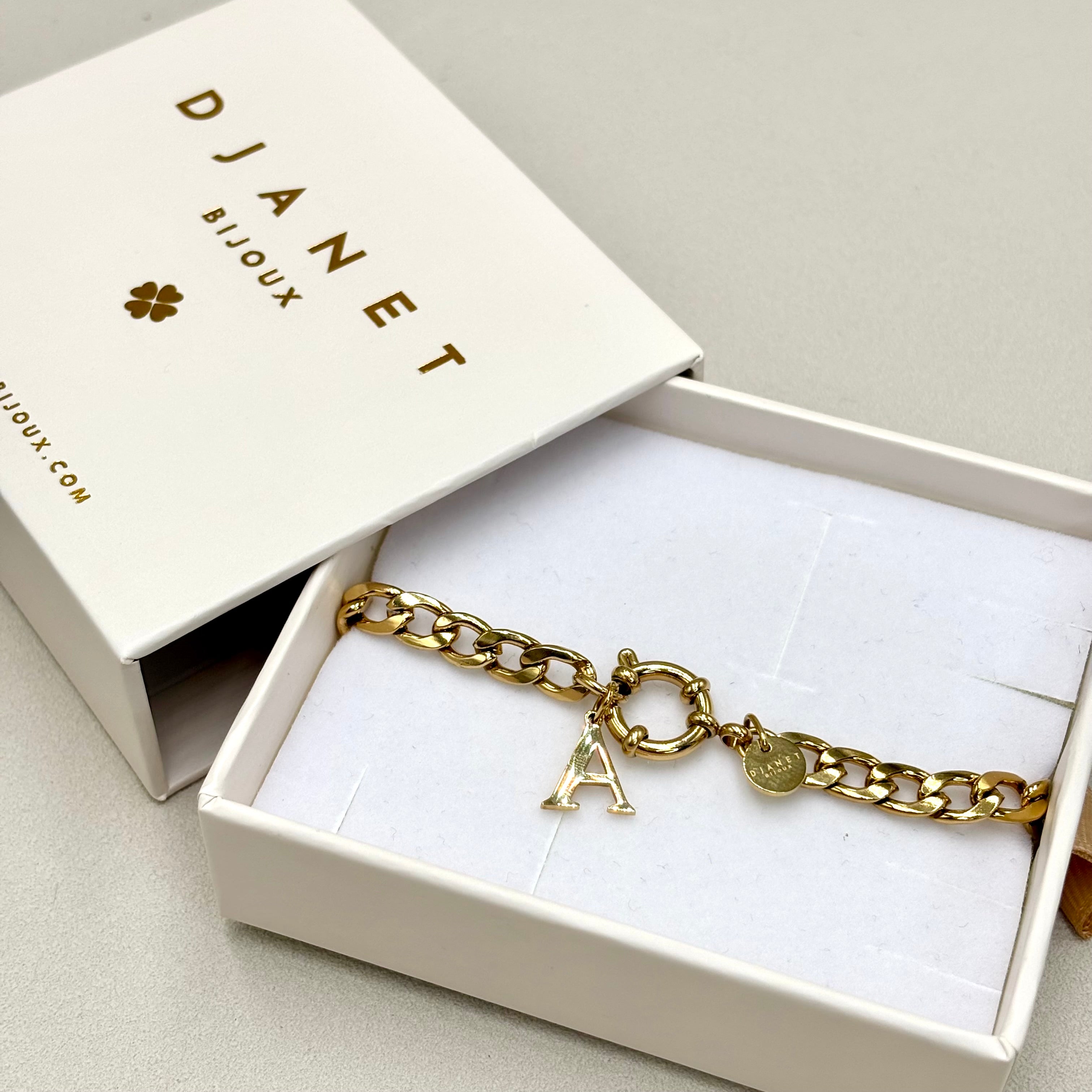 Bracelet gourmette en acier inoxydable doré avec fermoir mousqueton rond bouée et pendentif initiale présenté dans la boite cadeau Djanet Bijoux