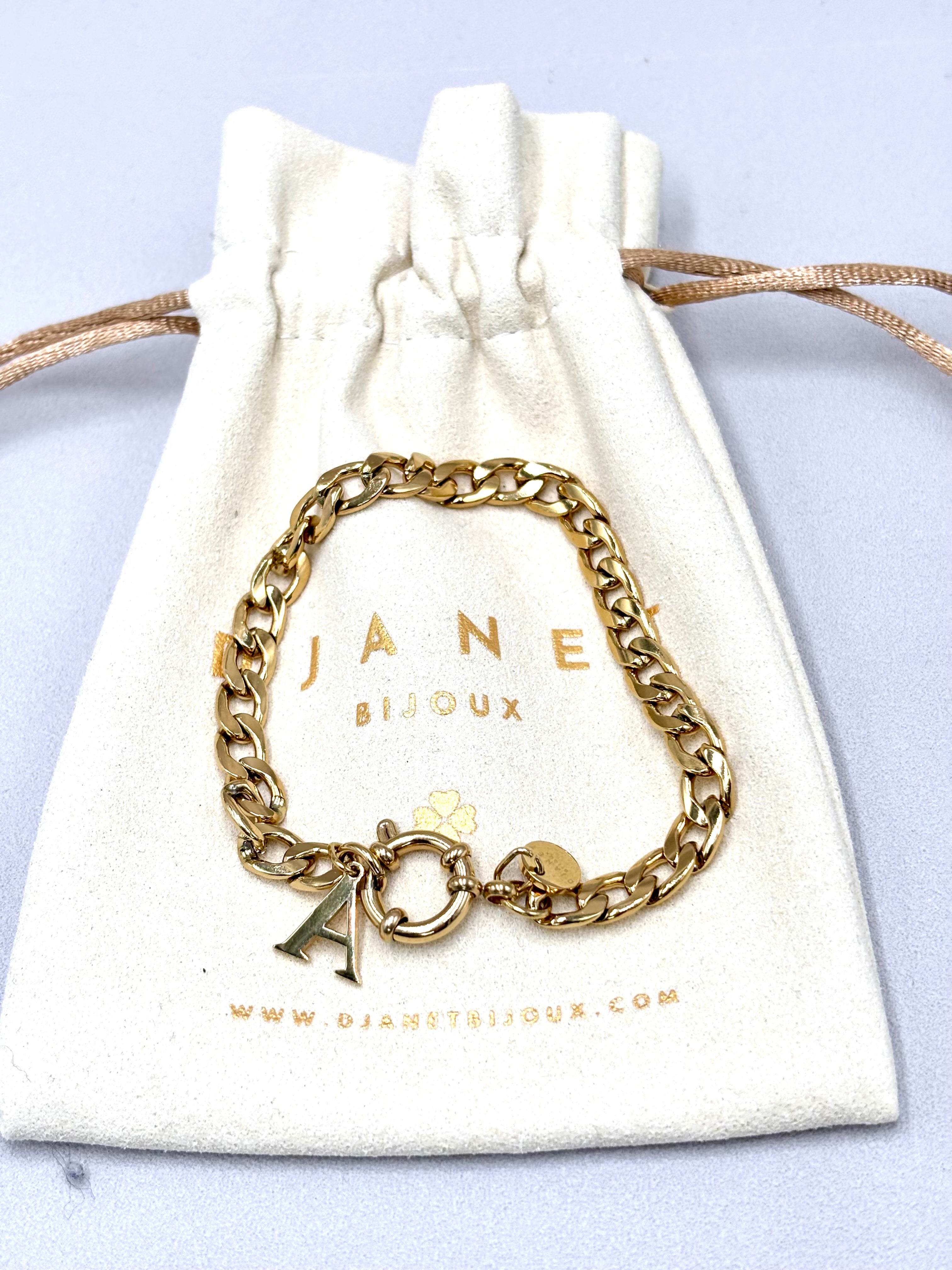 Bracelet gourmette en acier inoxydable doré avec fermoir mousqueton rond bouée et pendentif initiale présenté dans le pochon Djanet Bijoux