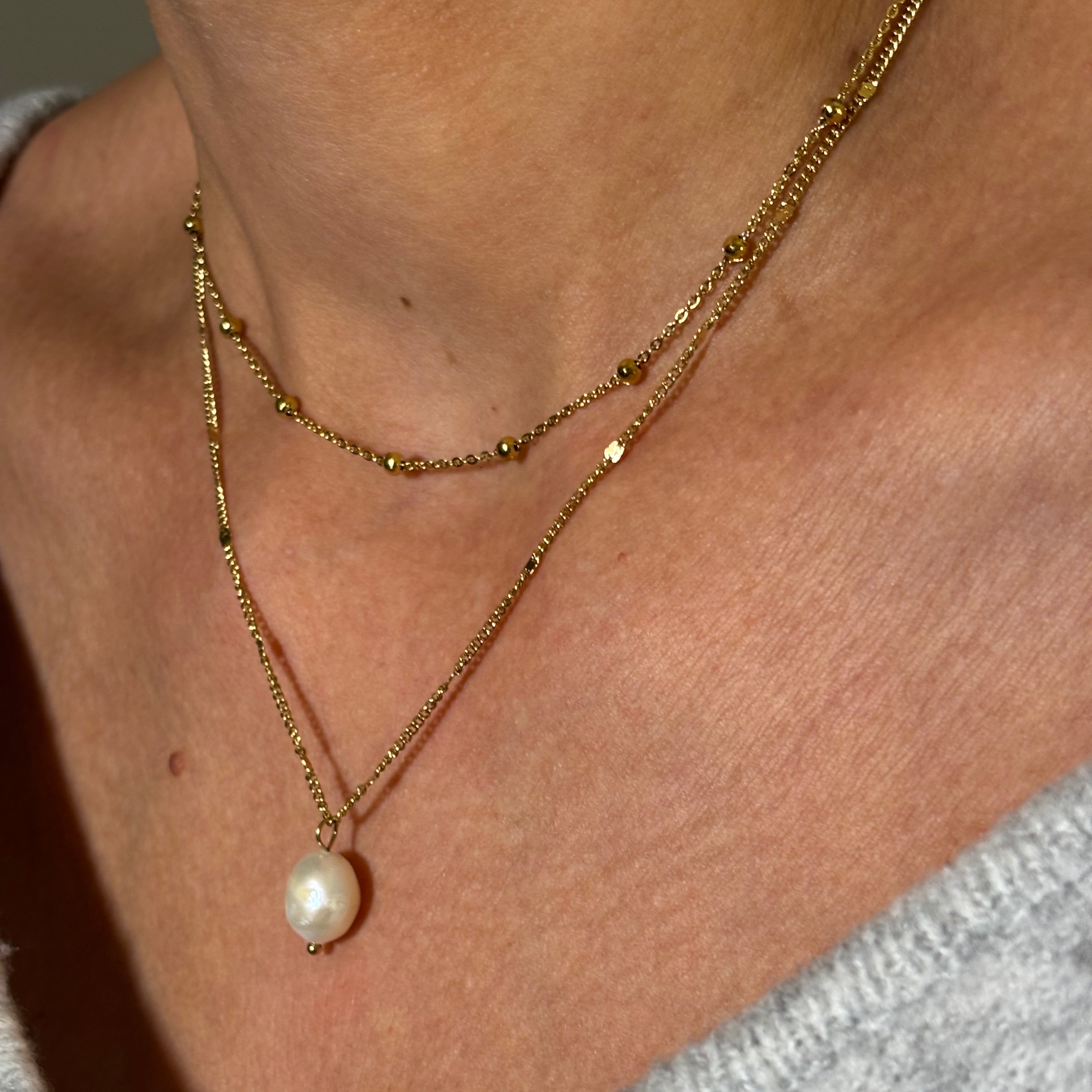 Gros plan sur Collier chaine fine en acier doré avec pendentif perles d'eau douce porté avec chaîne boules