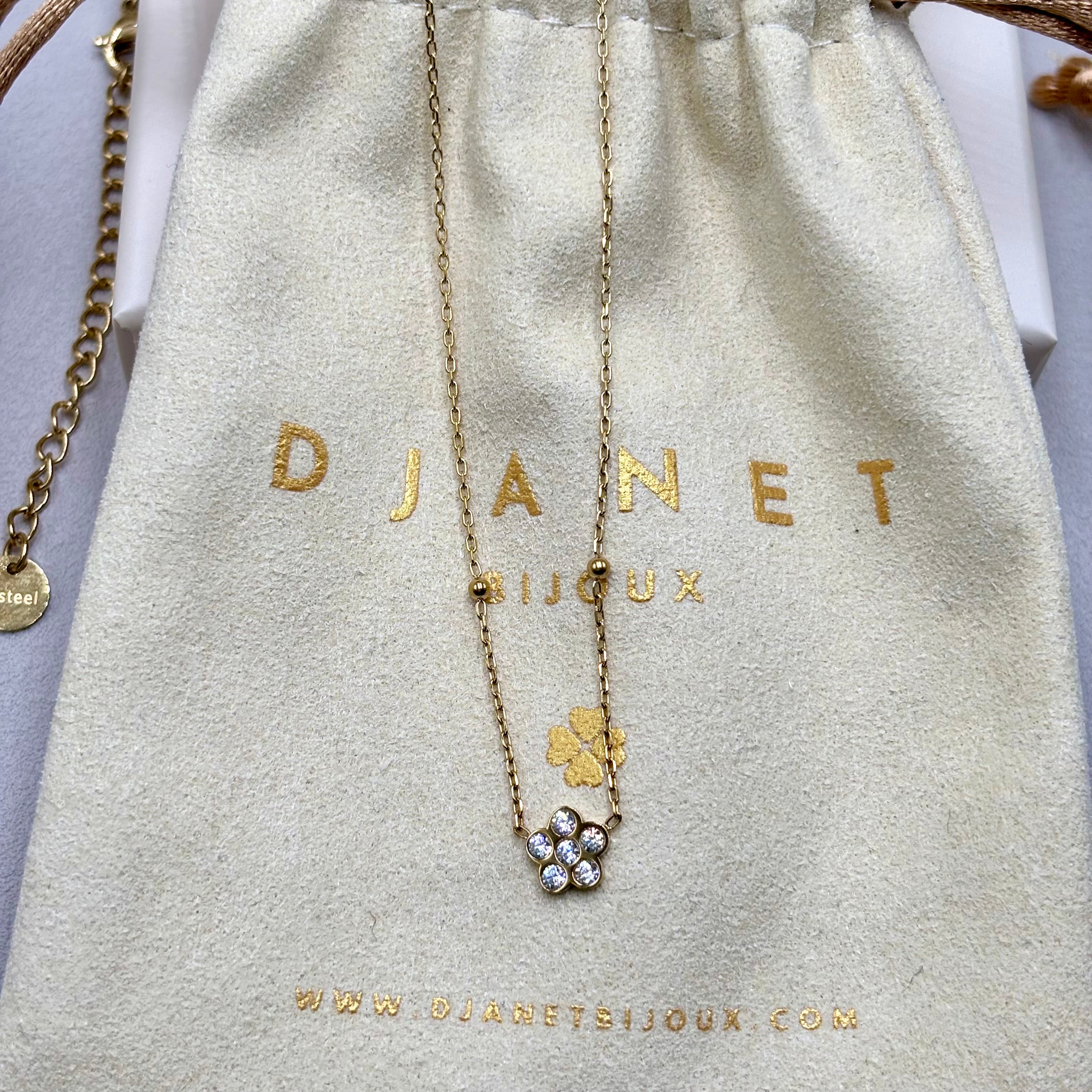Collier fin acier inoxydable doré à l'or fin orné d'une fleur en zirconium présenté sur pochon Djanet Bijoux