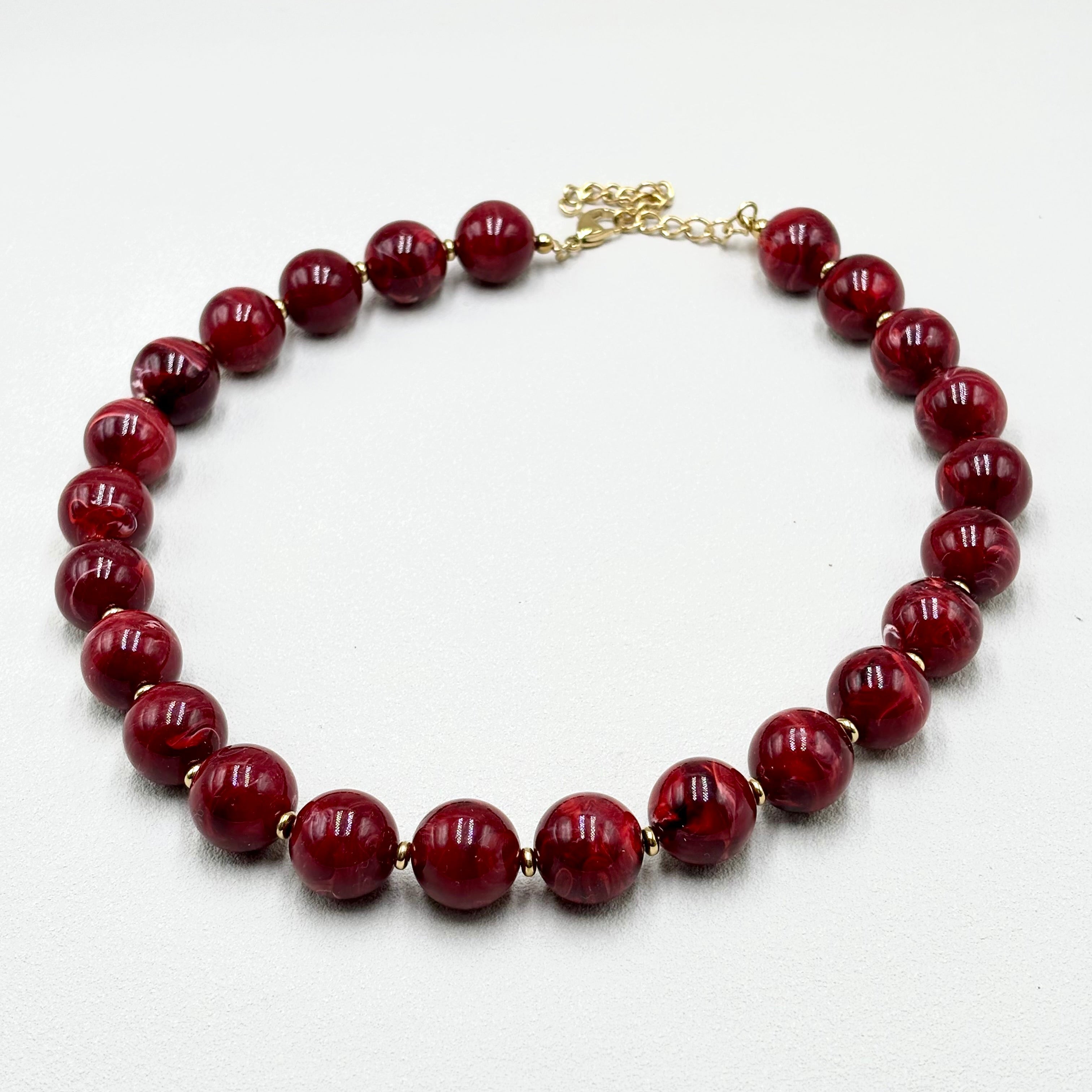 Collier grosses perles en résine rouge cerise et acier doré Perla sur fond blanc