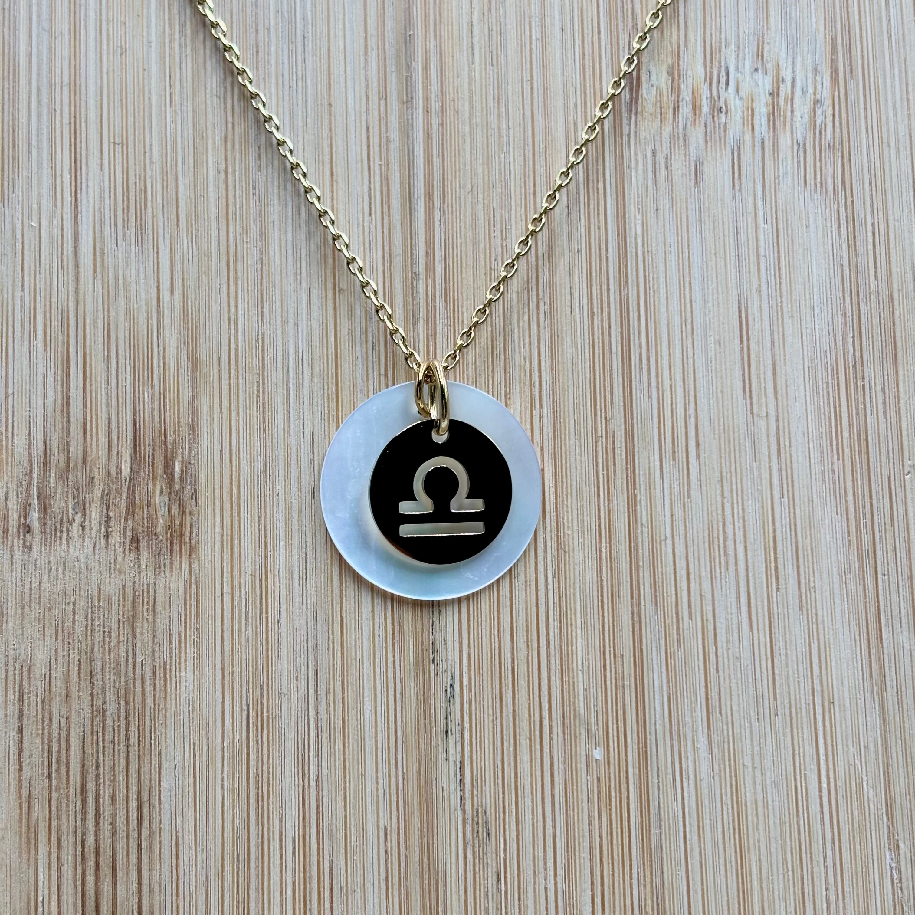 Collier personnalise signe Astro balance sur chaine maille forçat acier dore et medaille ronde en nacre présenté sur fond bois