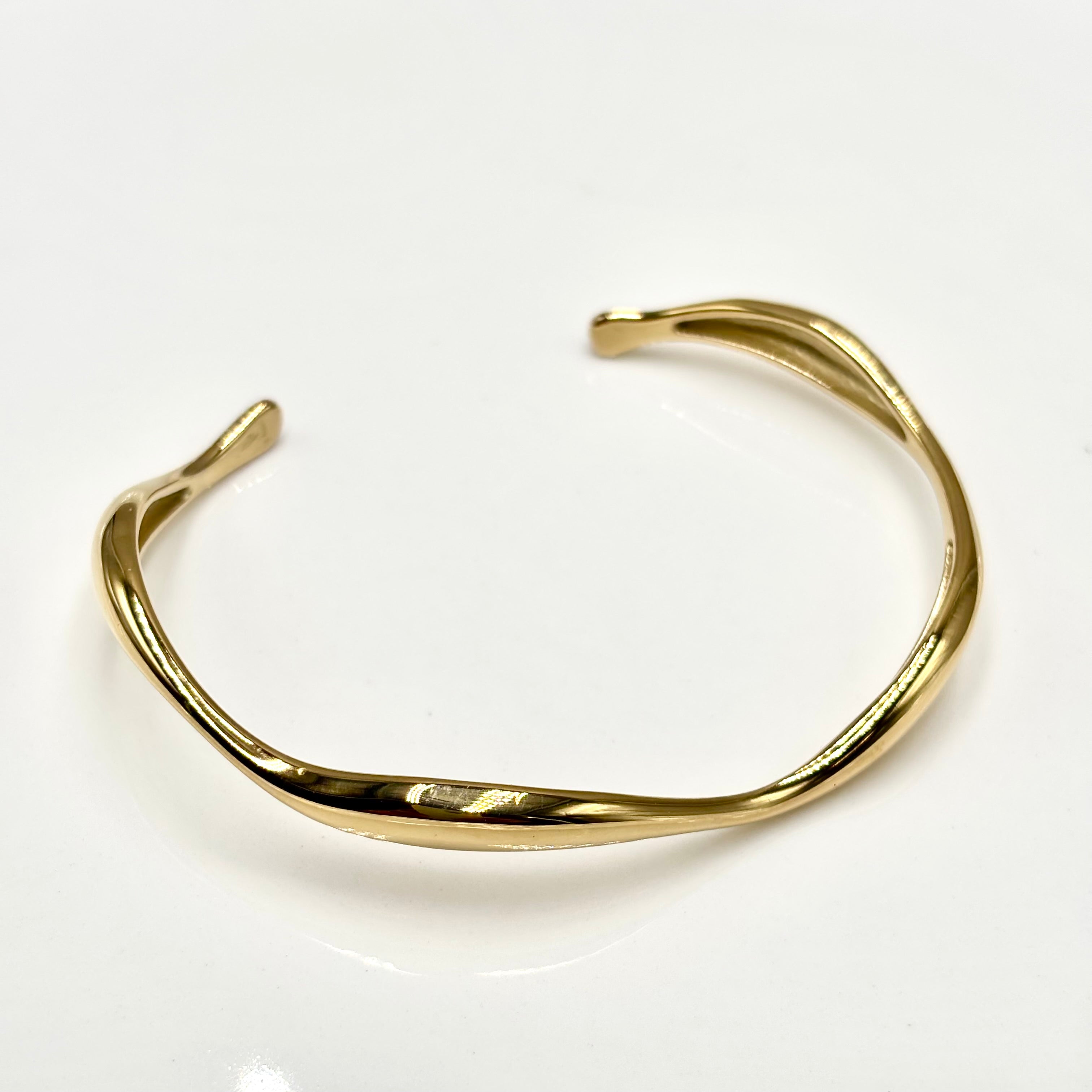 Jonc ondulé en acier inoxydable doré ouvert sur fond blanc