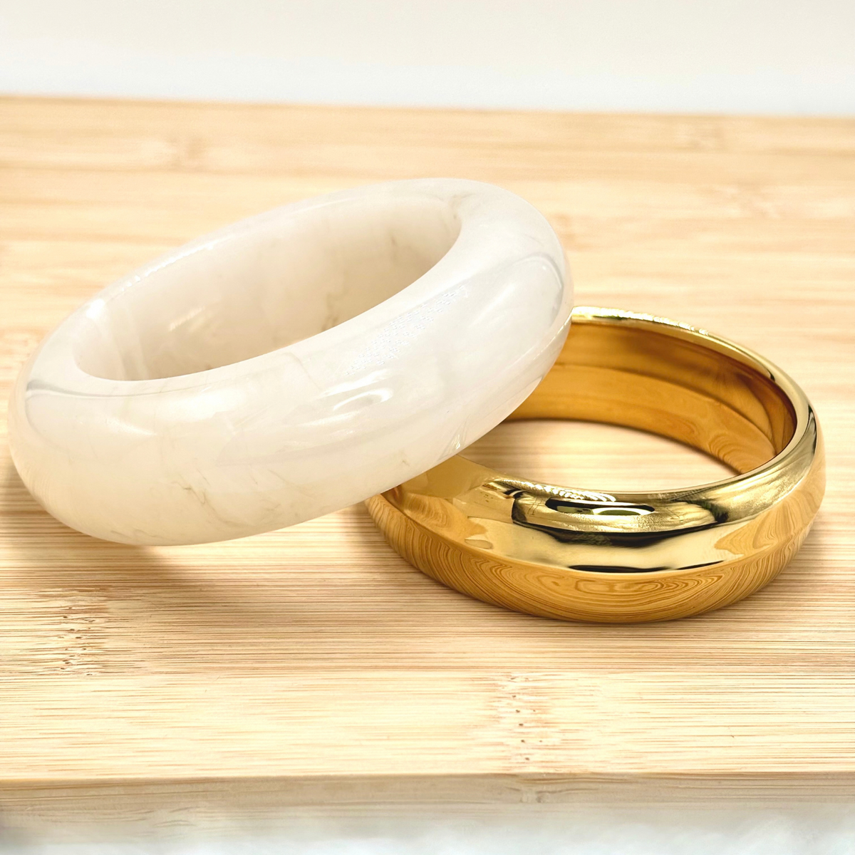 Deux bracelets manchette large en acier doré et bracelet jonc épais en résine blanc