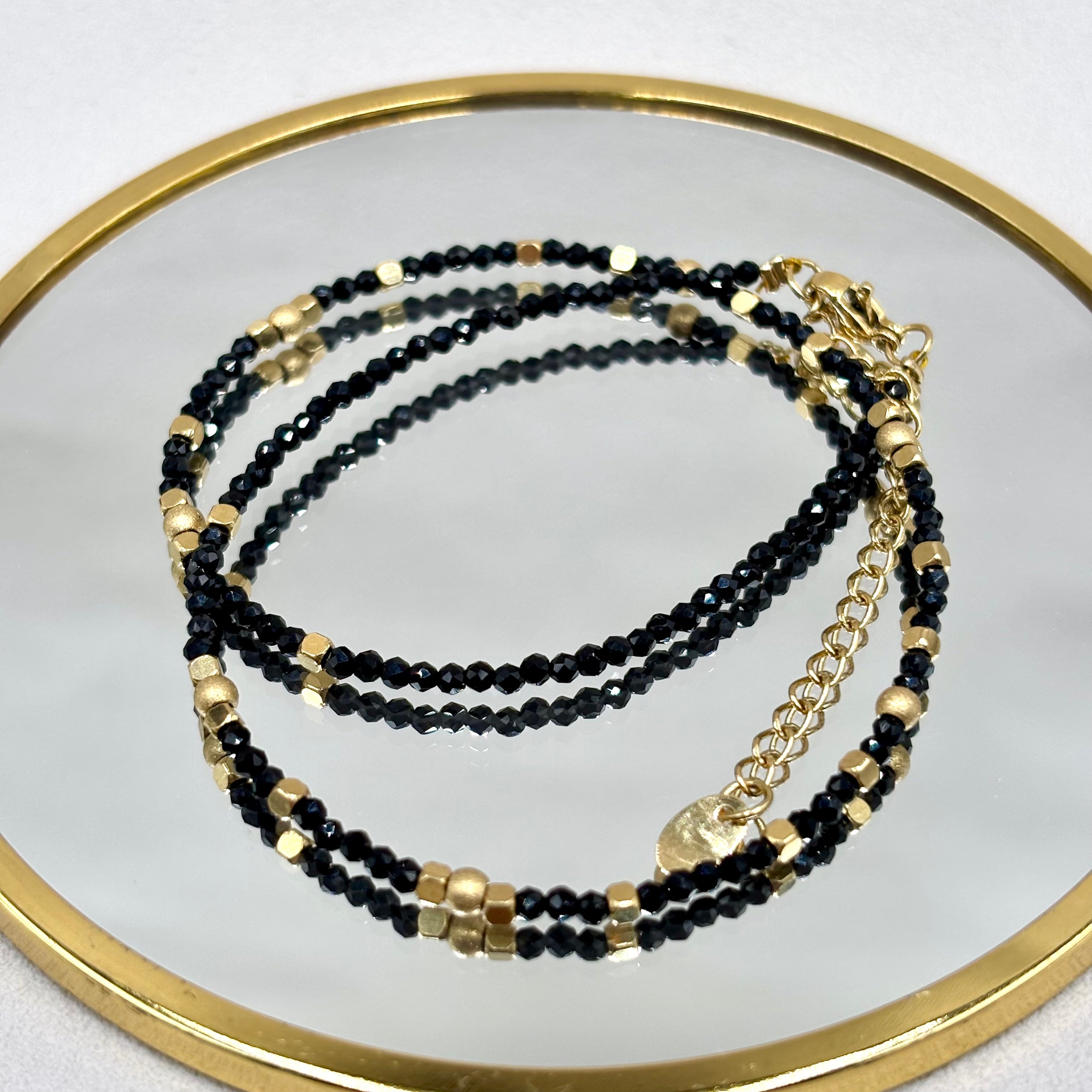 Bracelet Deira en onyx orné de perles d'acier inoxydable et d'hématites dorées présenté sur un miroir