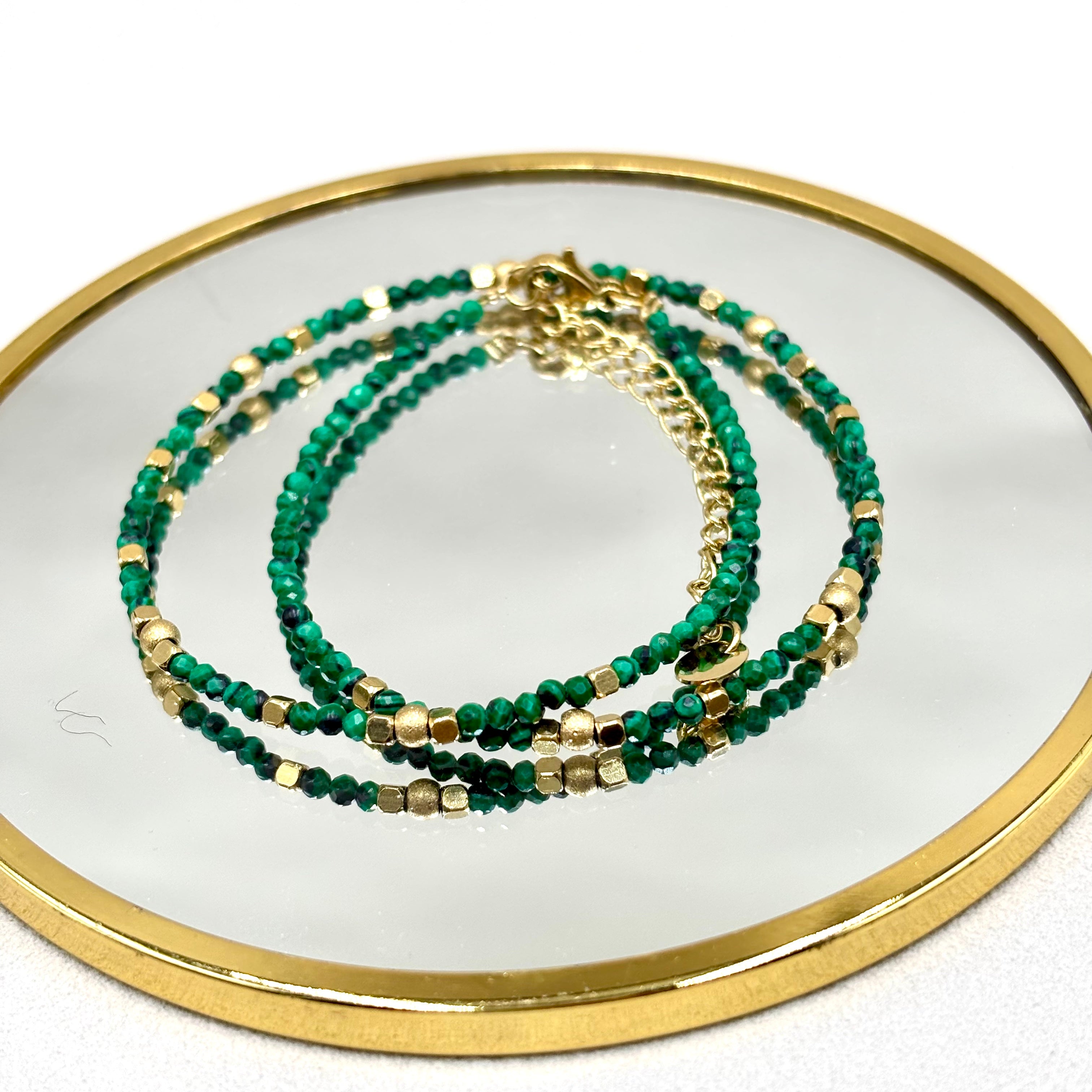 Bracelet Deira en malachite orné de perles d'acier inoxydable et d'hématites dorées présenté sur un miroir