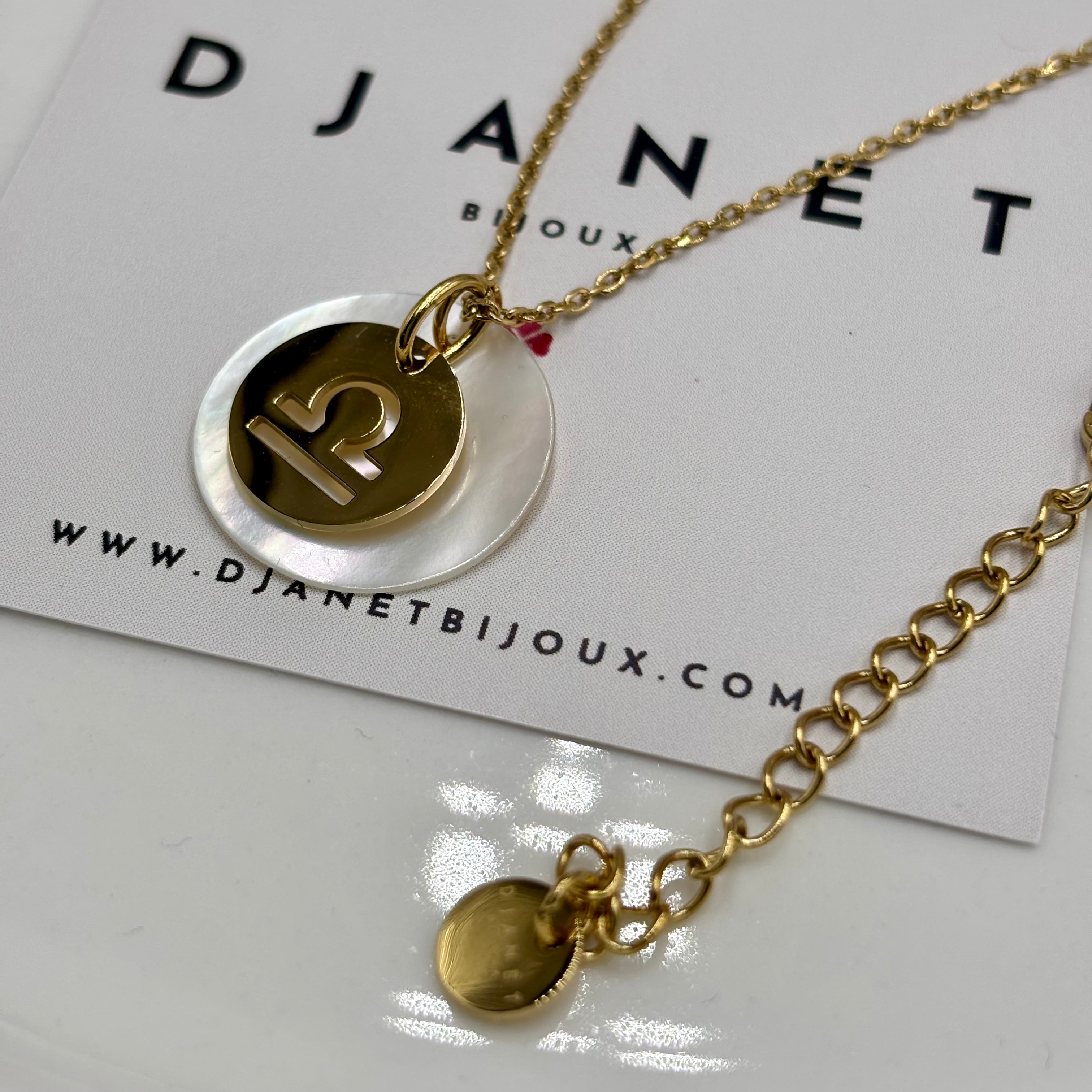 Collier personnalise signe Astro balance sur chaine maille forçat acier dore et medaille ronde en nacre présenté sur carte Djanet Bijoux